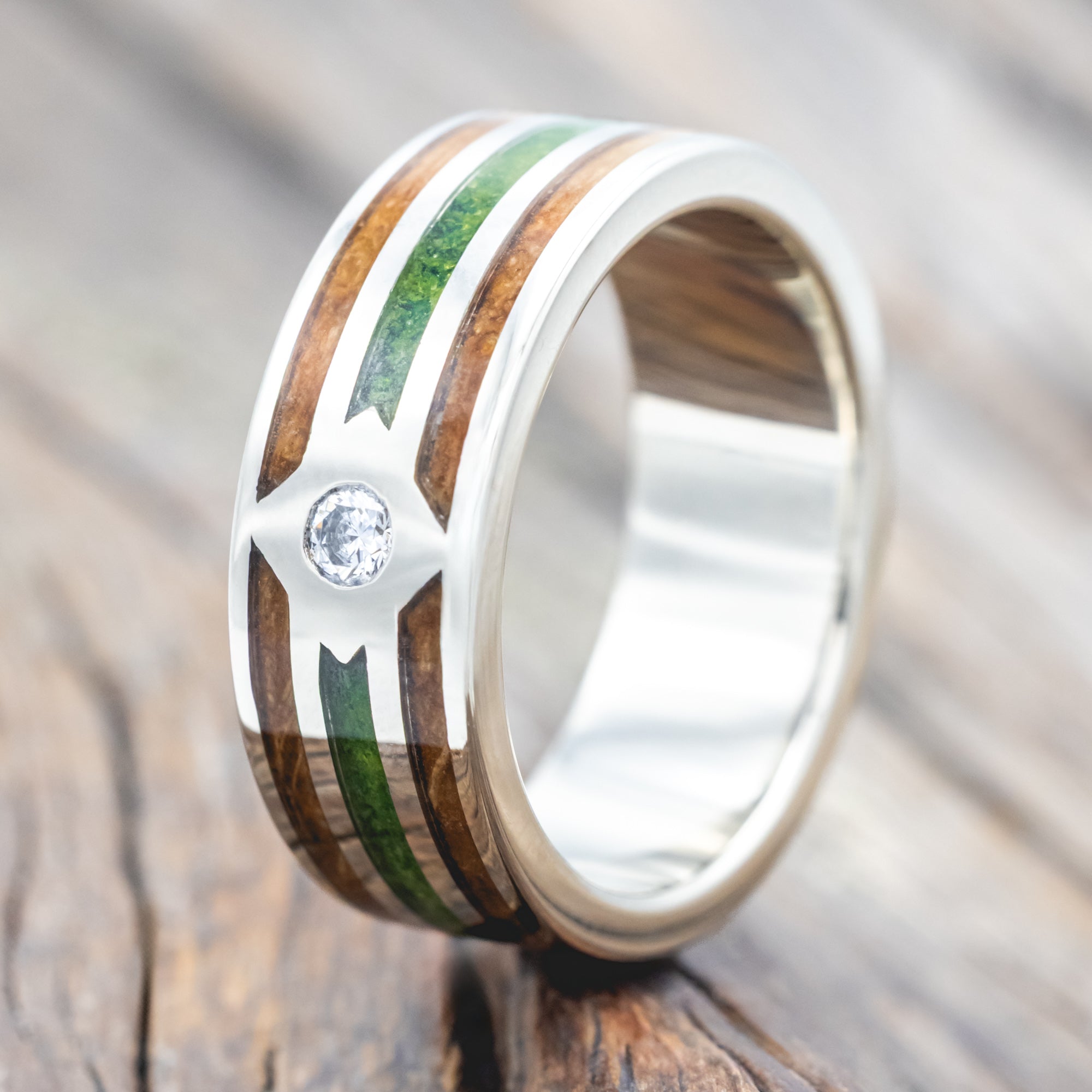 White gold ring with whiskey barrel oak and moss inlay and diamond accent on a wooden surface