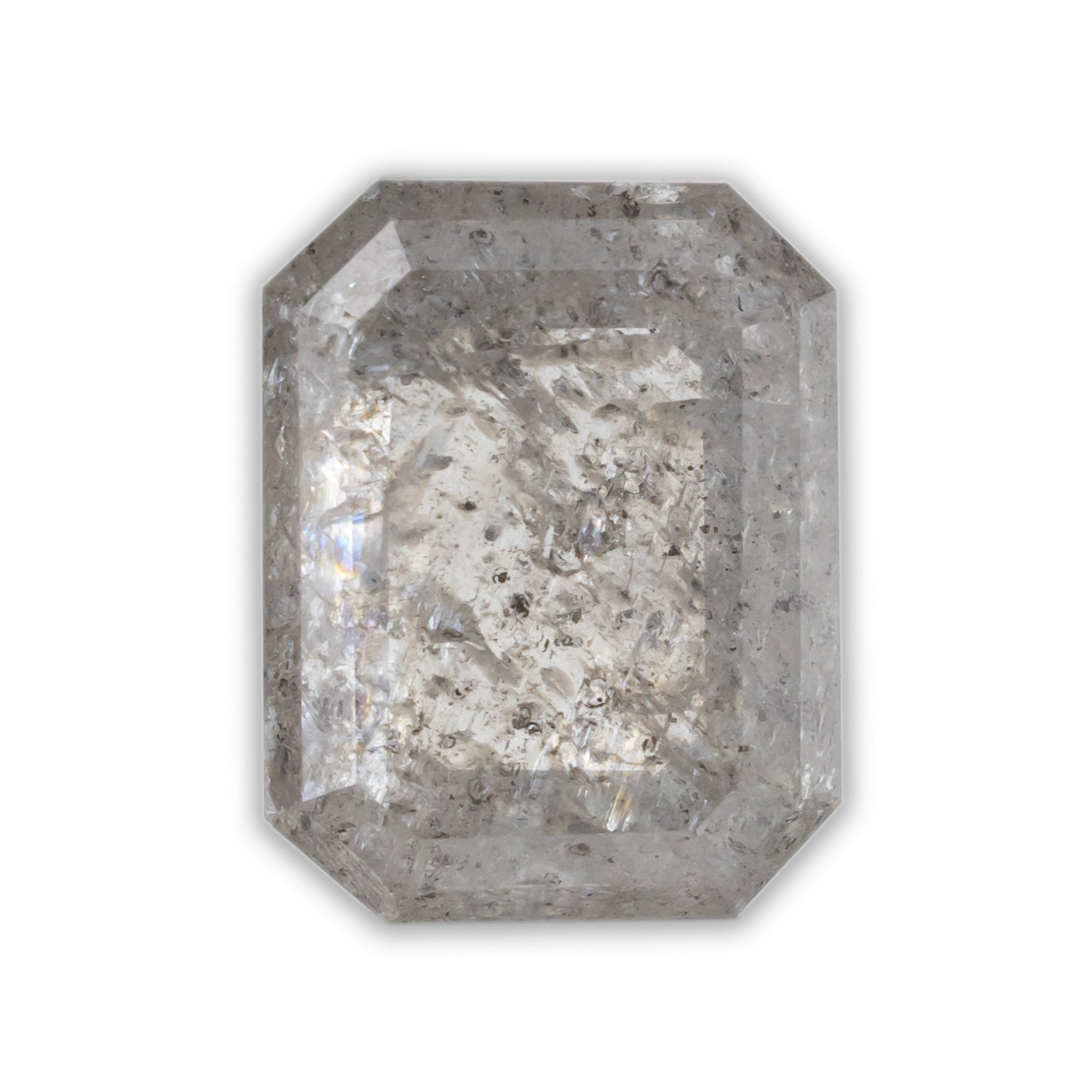An emerald cut salt & pepper diamond with grey inclusions throughout the stone, on a white background