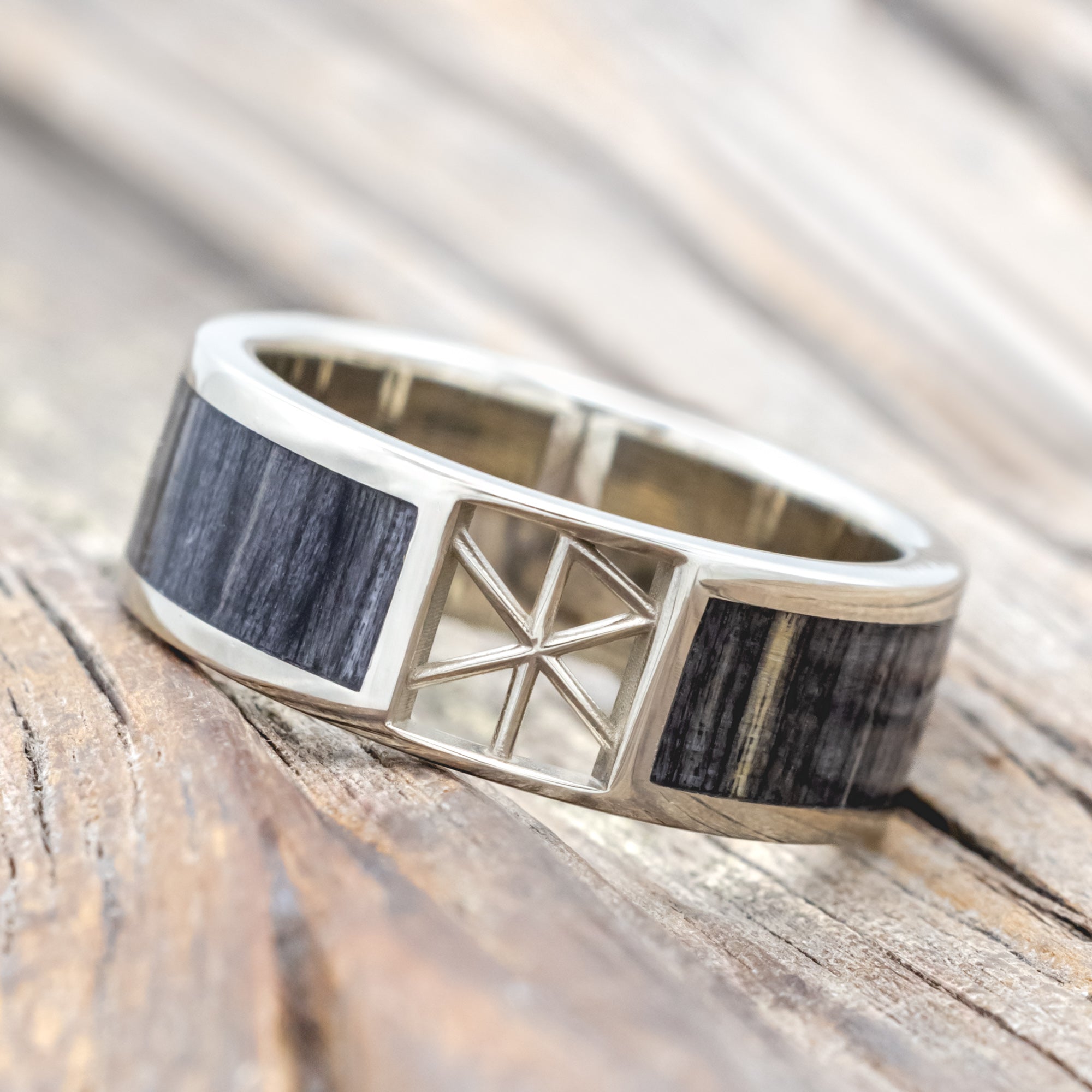 White gold ring with wooden inlay and rune cutout on a wooden surface