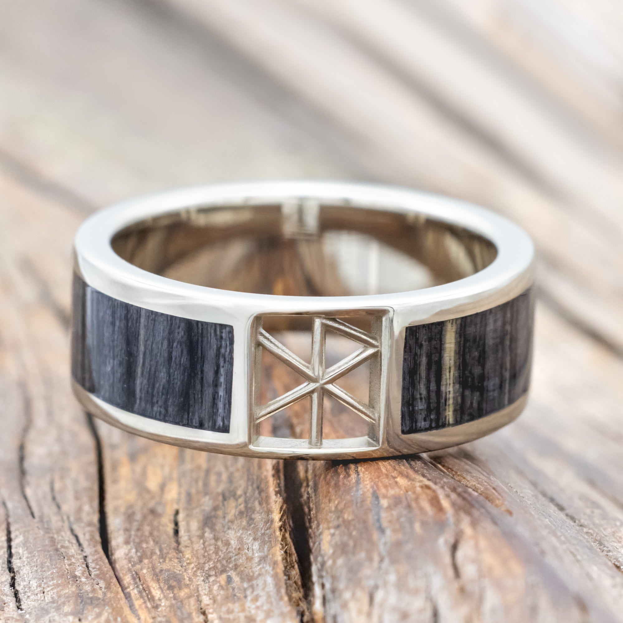 White gold ring with wooden inlay and rune cutout on a wooden surface