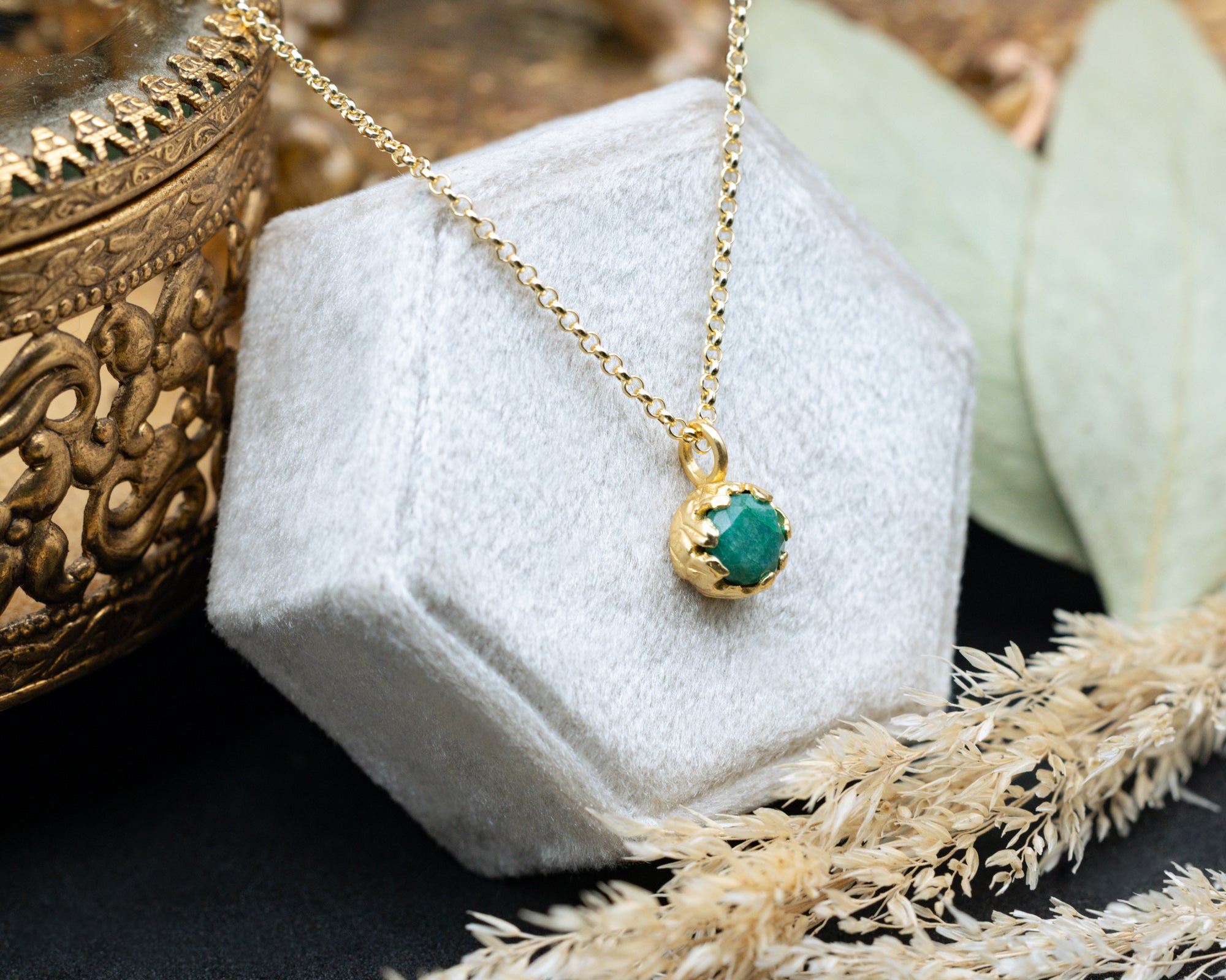 Gold necklace with a green pendant on a white stand, surrounded by decorative elements.