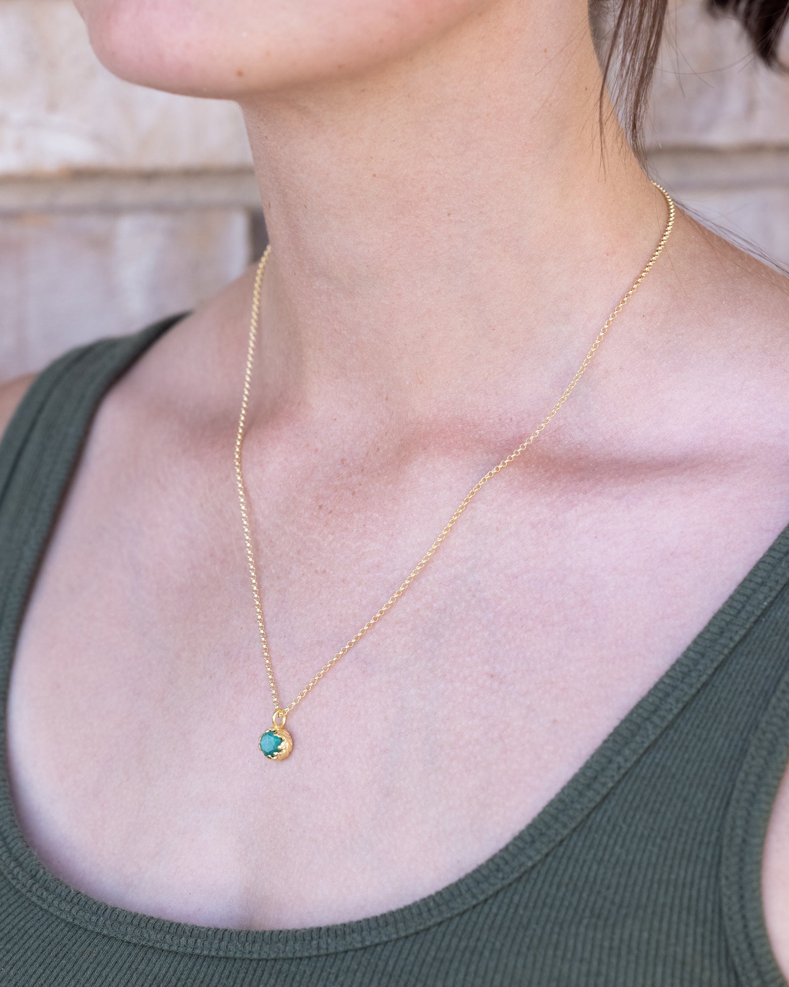 Gold necklace with a green emerald worn by a person in a green tank top.