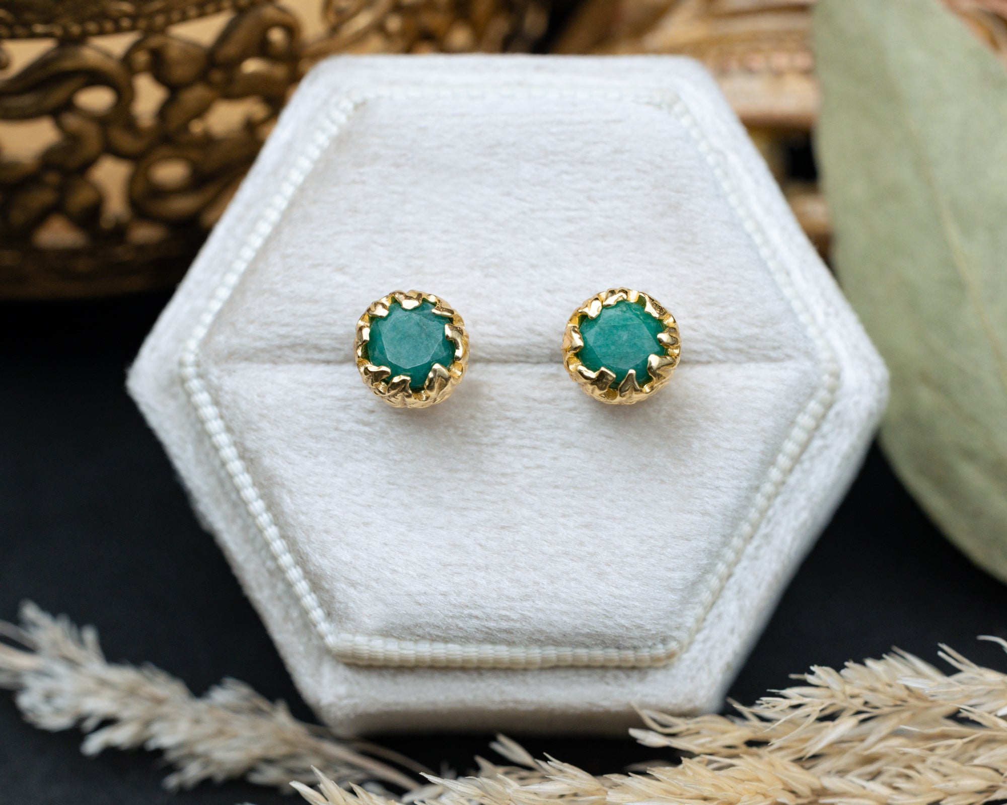 Pair of emerald stud earrings with gold accents on a white hexagonal jewelry box.