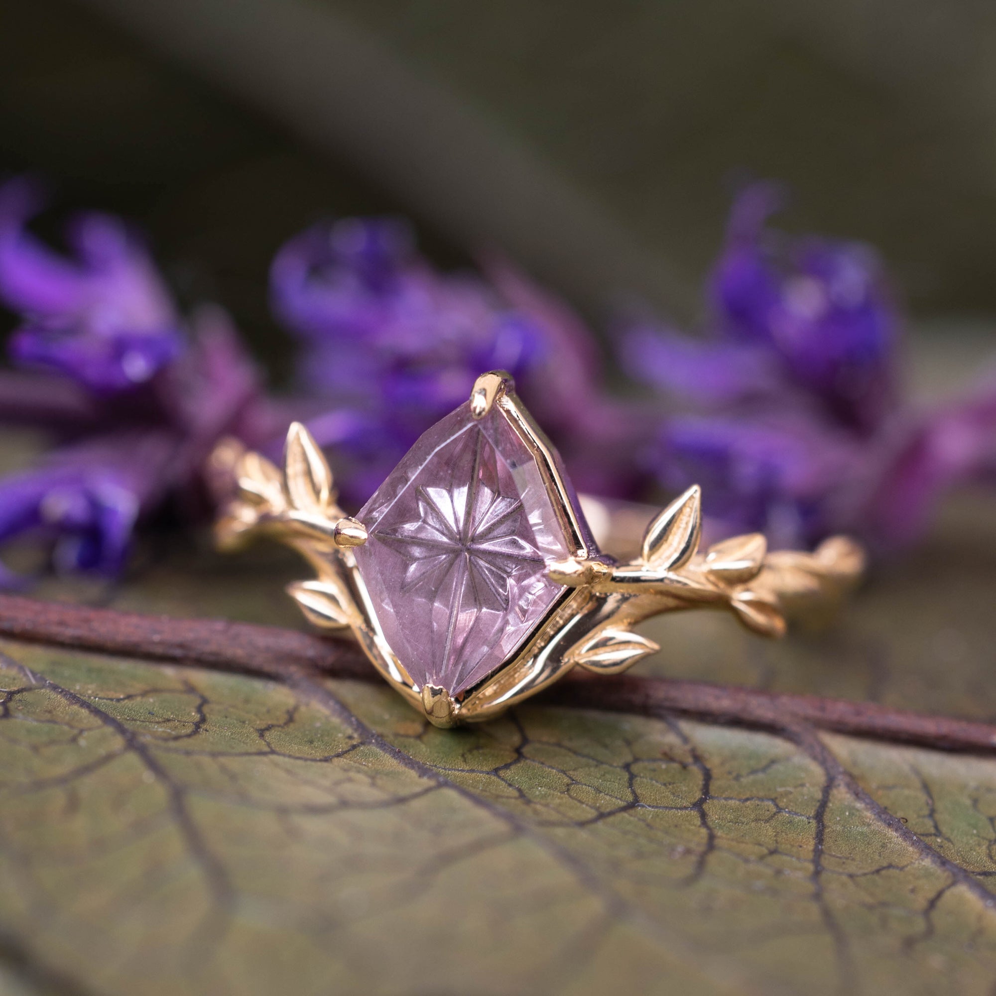 Gold ring with a pink garnet on a leaf with purple flowers in the background