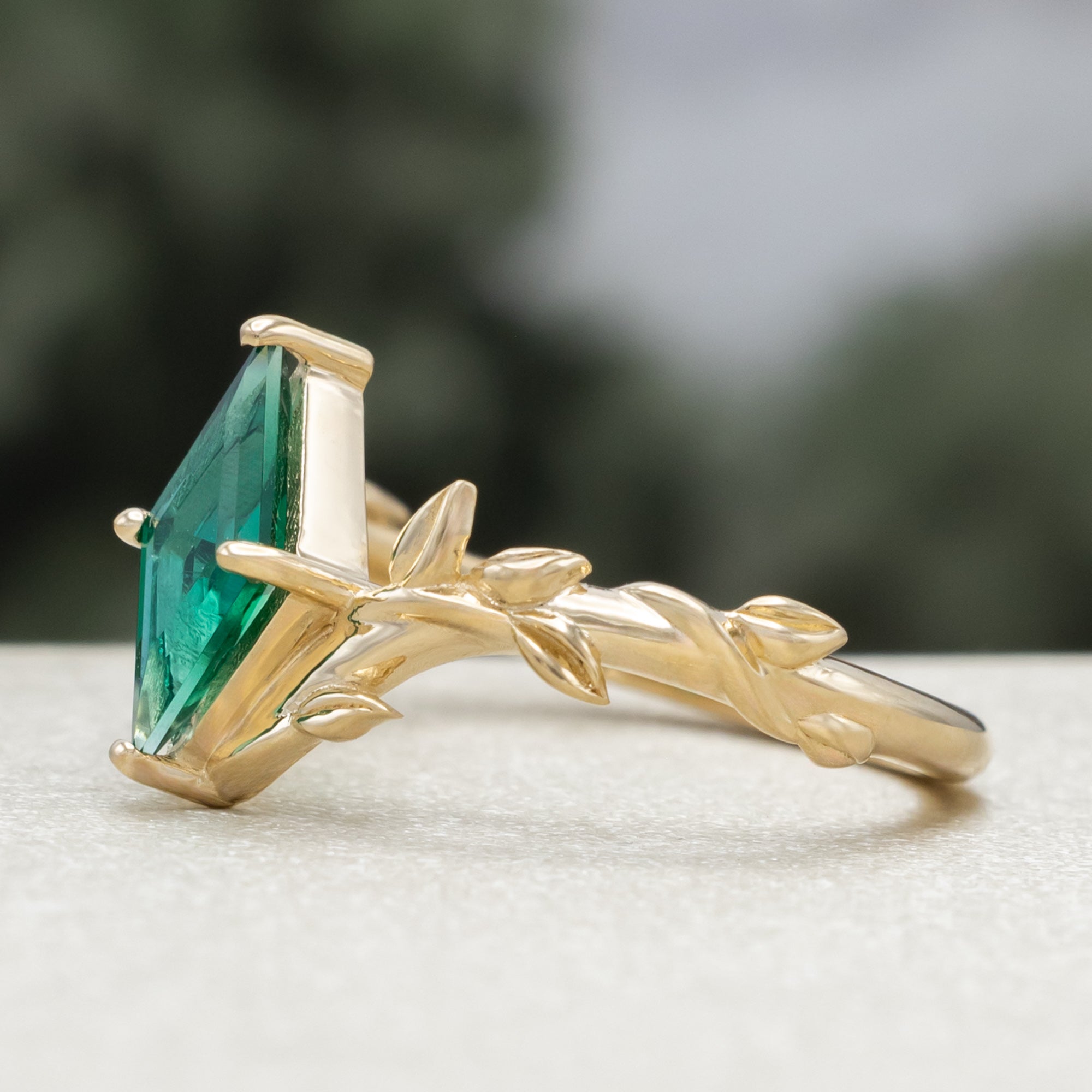 Gold ring with a lozenge emerald and leaf filigree on a blurred background