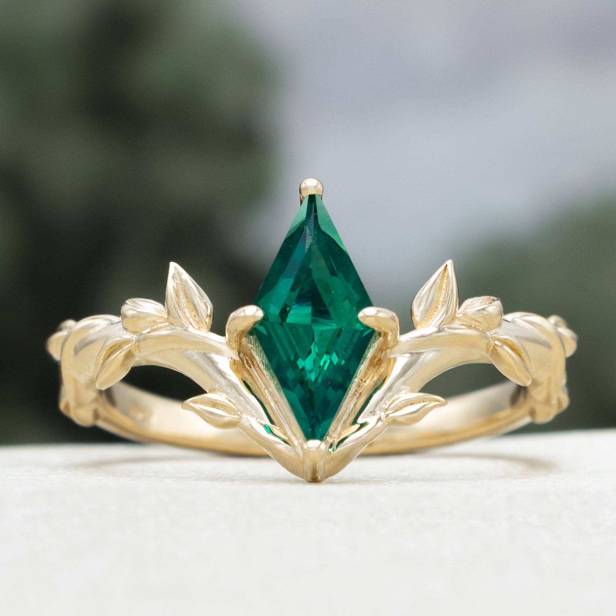 Gold ring with a lozenge emerald and leaf filigree on a blurred background