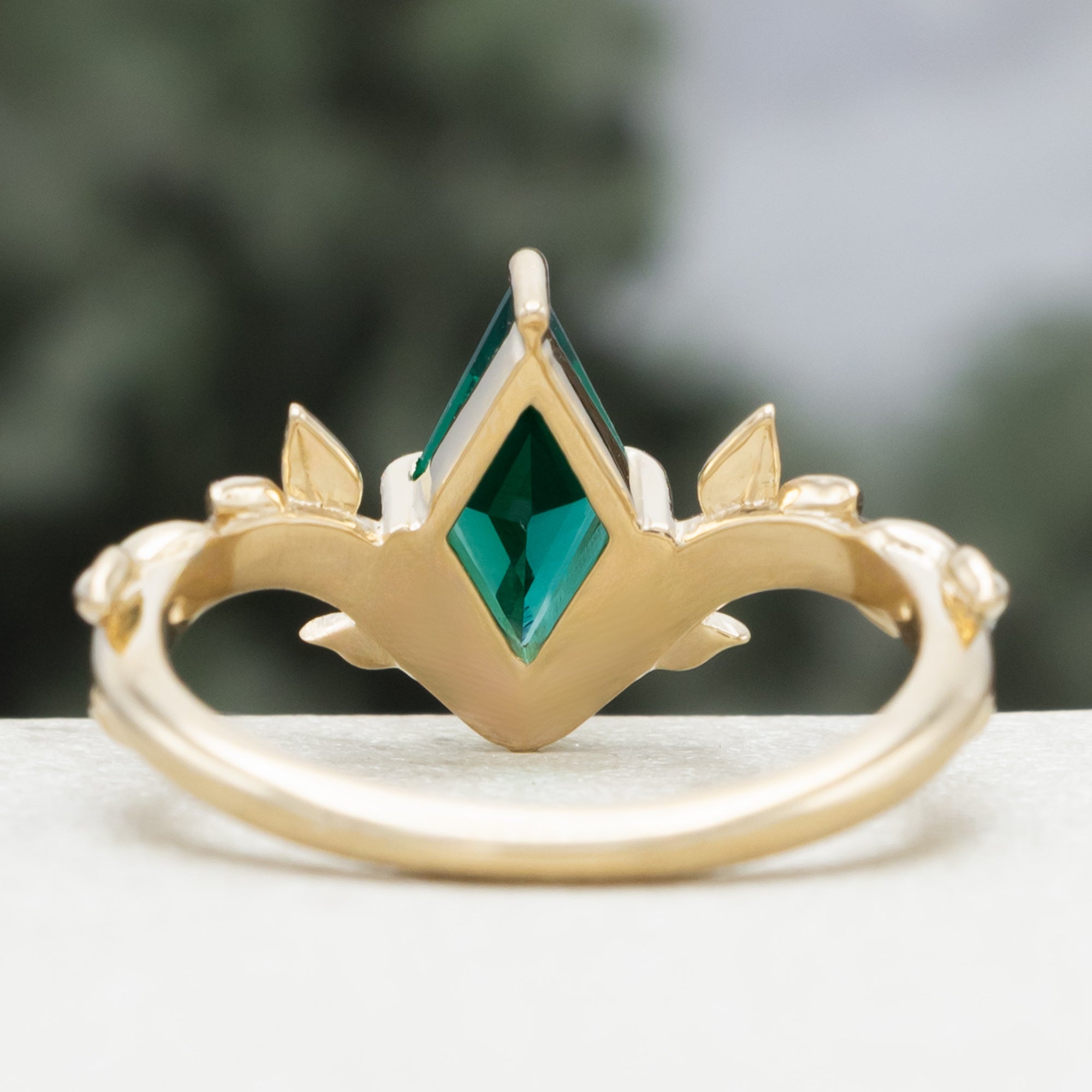 Gold ring with a lozenge emerald and leaf filigree on a blurred background