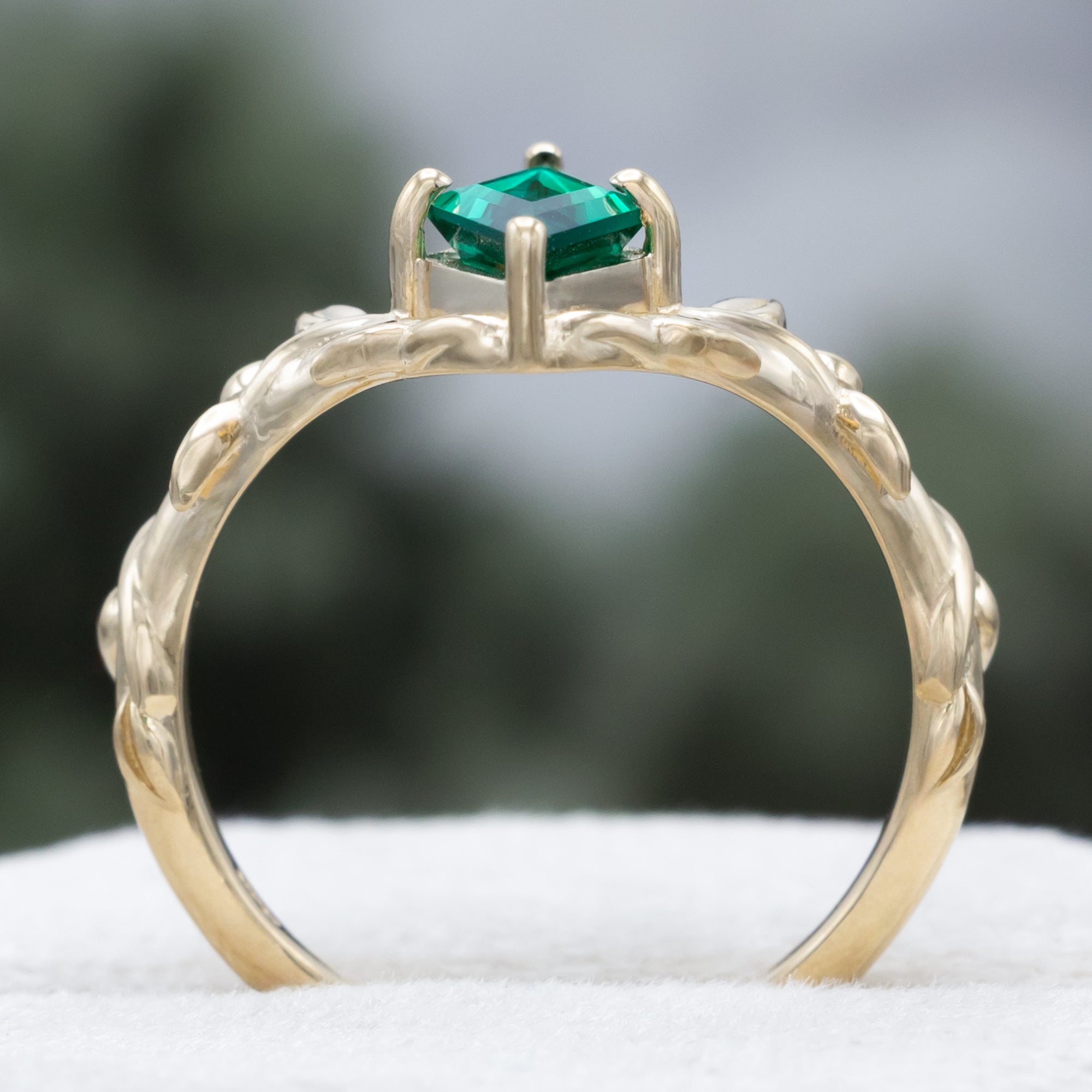 Gold ring with a lozenge emerald and leaf filigree on a blurred background