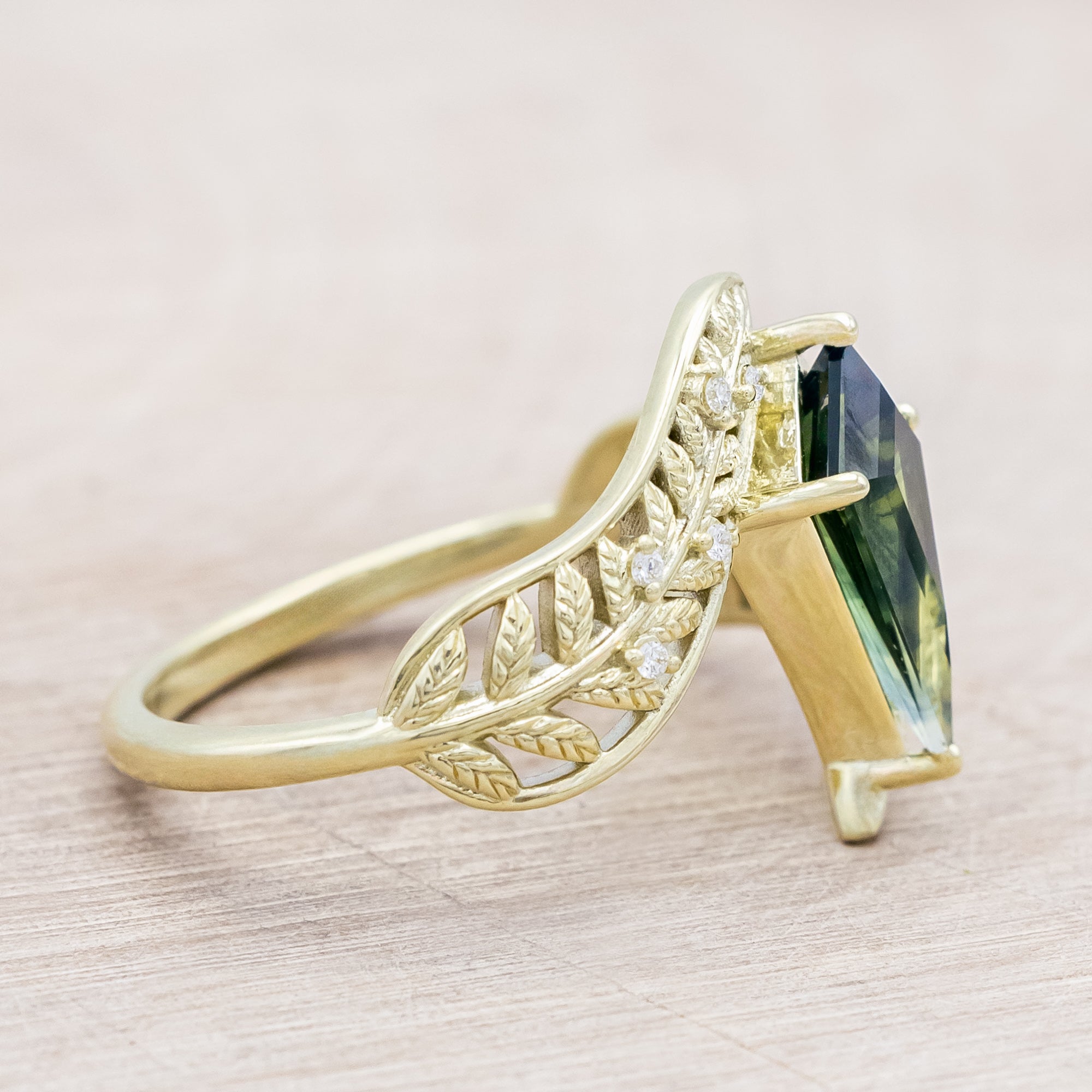 Green gold ring with a green sapphire on a light wooden surface