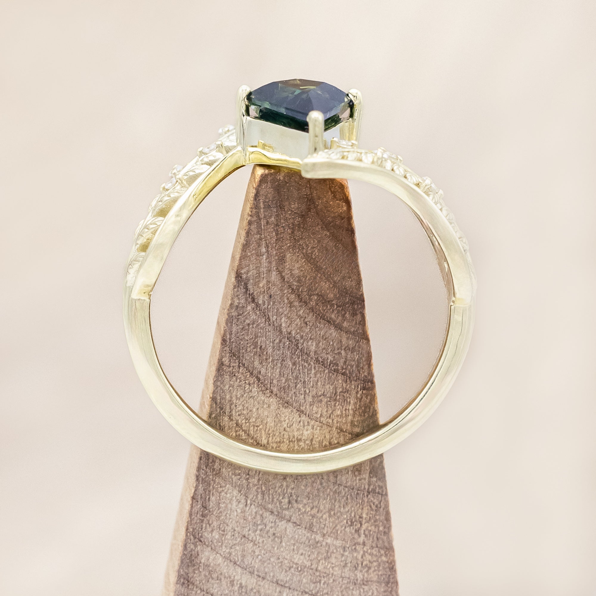 Green gold ring with a green sapphire on a wooden stand against a beige background