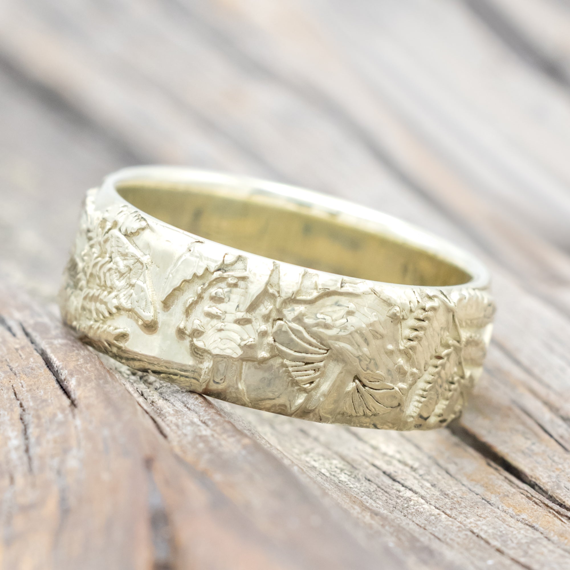 Green gold ring with intricate engravings on a wooden surface