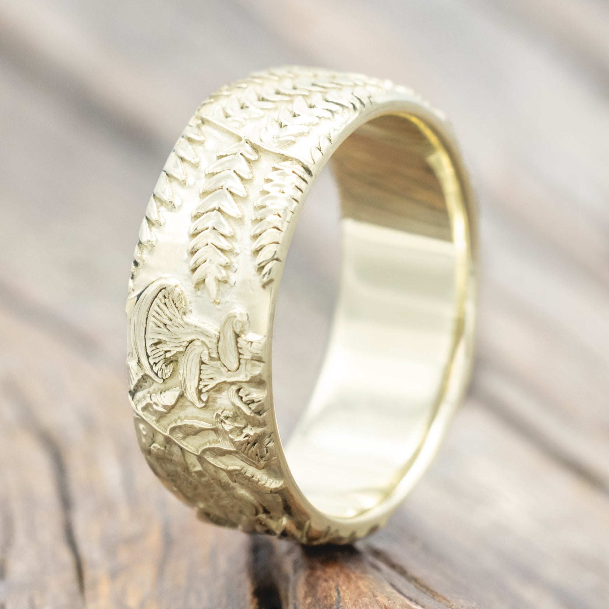 Green gold ring with intricate engravings on a wooden surface