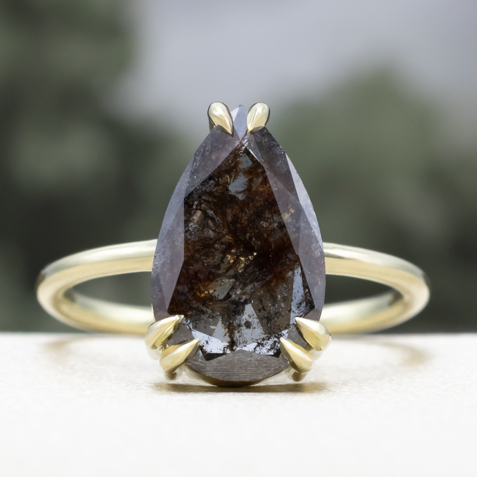 Solitaire green gold ring with a pear salt & pepper diamond centerstone against a blurred background