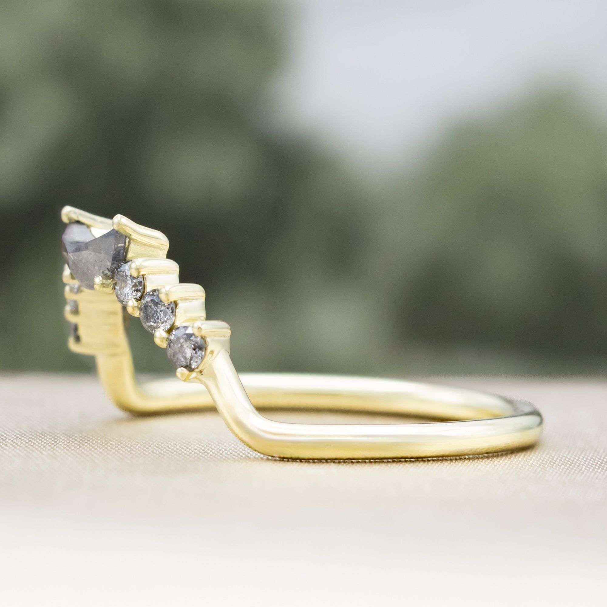 Green gold ring with salt & pepper diamond accents on a neutral background