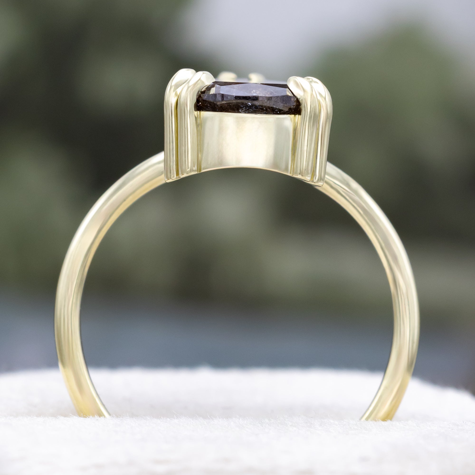Solitaire green gold ring with a pear salt & pepper diamond centerstone against a blurred background
