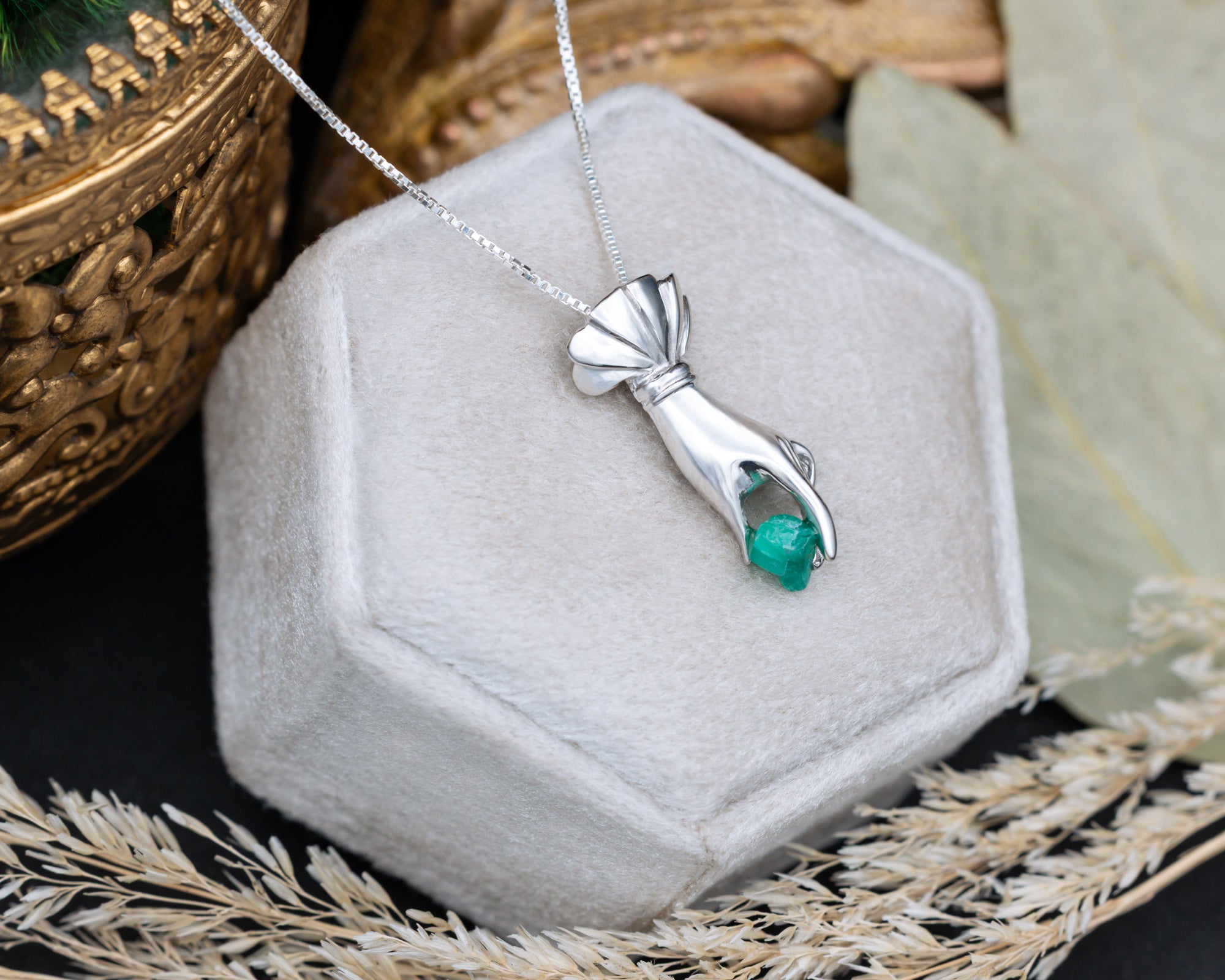 Silver hand pendant with a raw emerald in a hexagonal jewelry box.