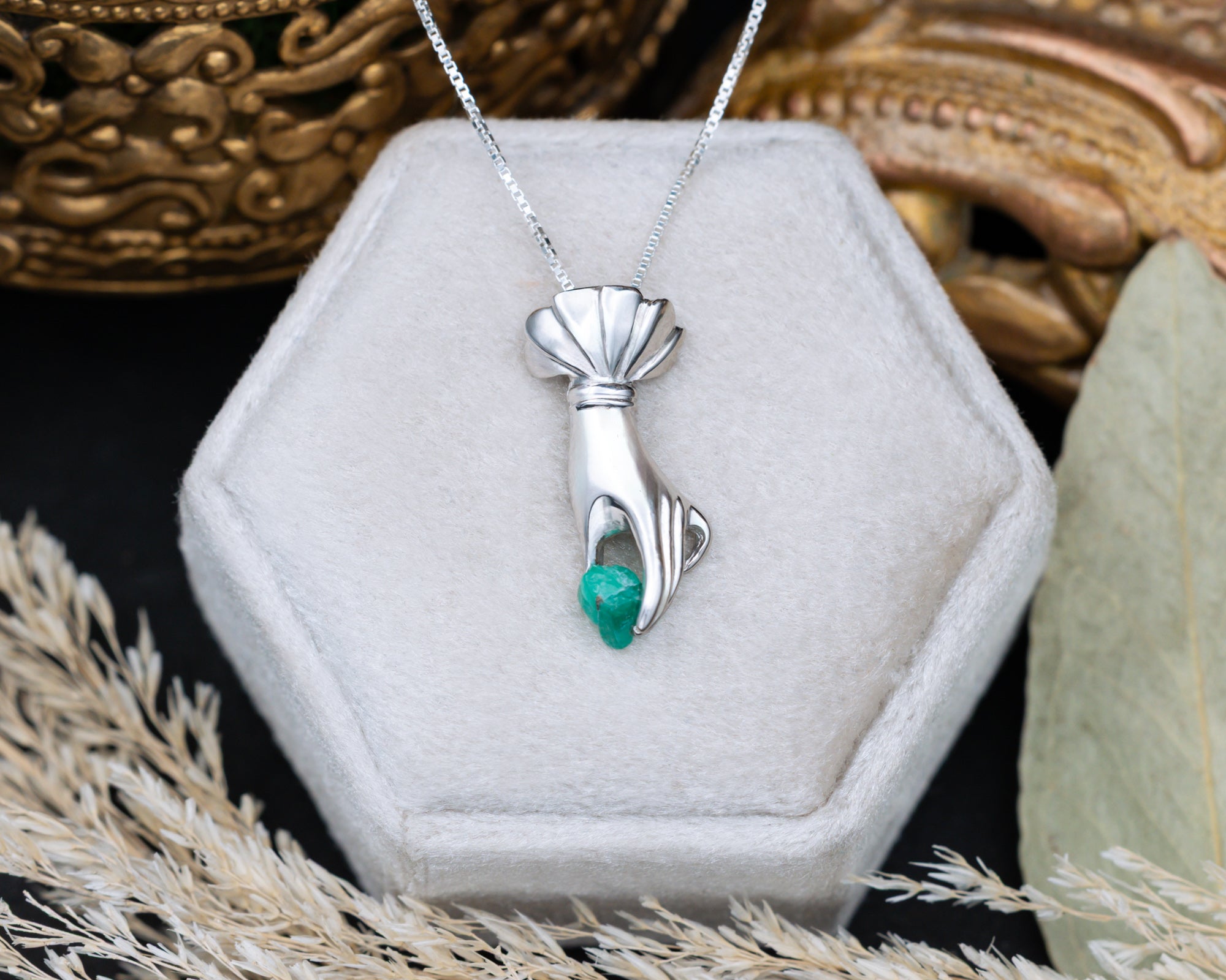 Silver hand pendant with a raw emerald in a hexagonal jewelry box.