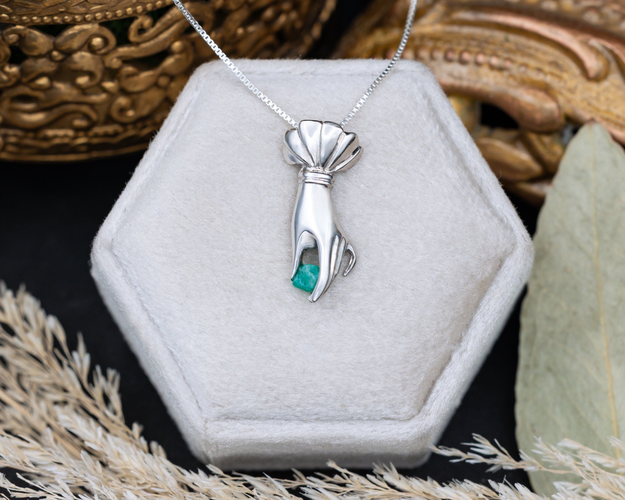 Silver hand pendant with a raw emerald in a hexagonal jewelry box.