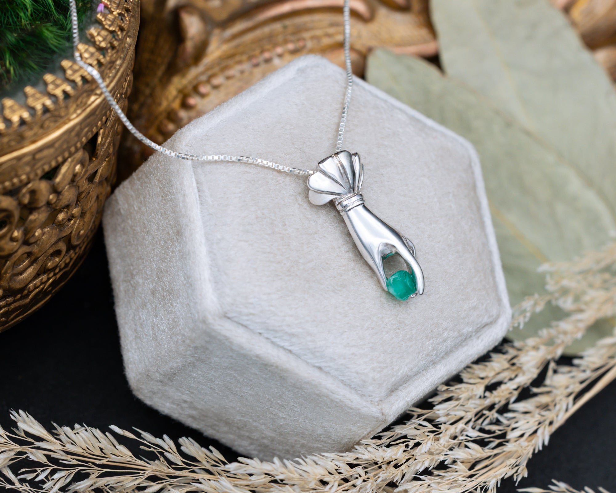 Silver hand pendant with a raw emerald in a hexagonal jewelry box.