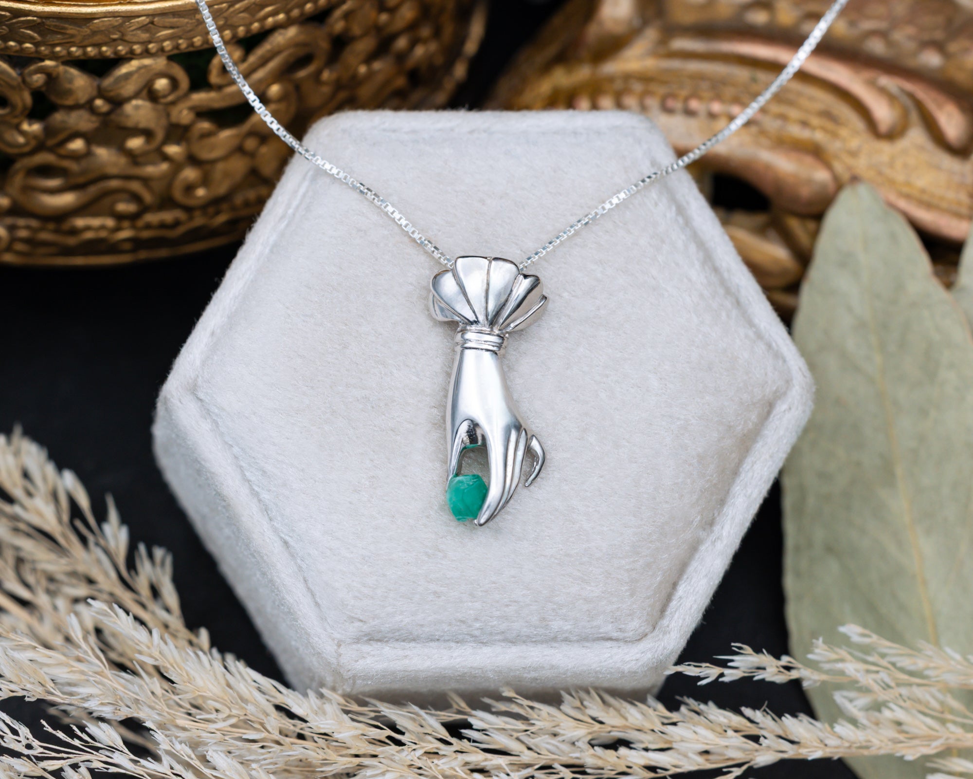Silver hand pendant with a raw emerald in a hexagonal jewelry box.