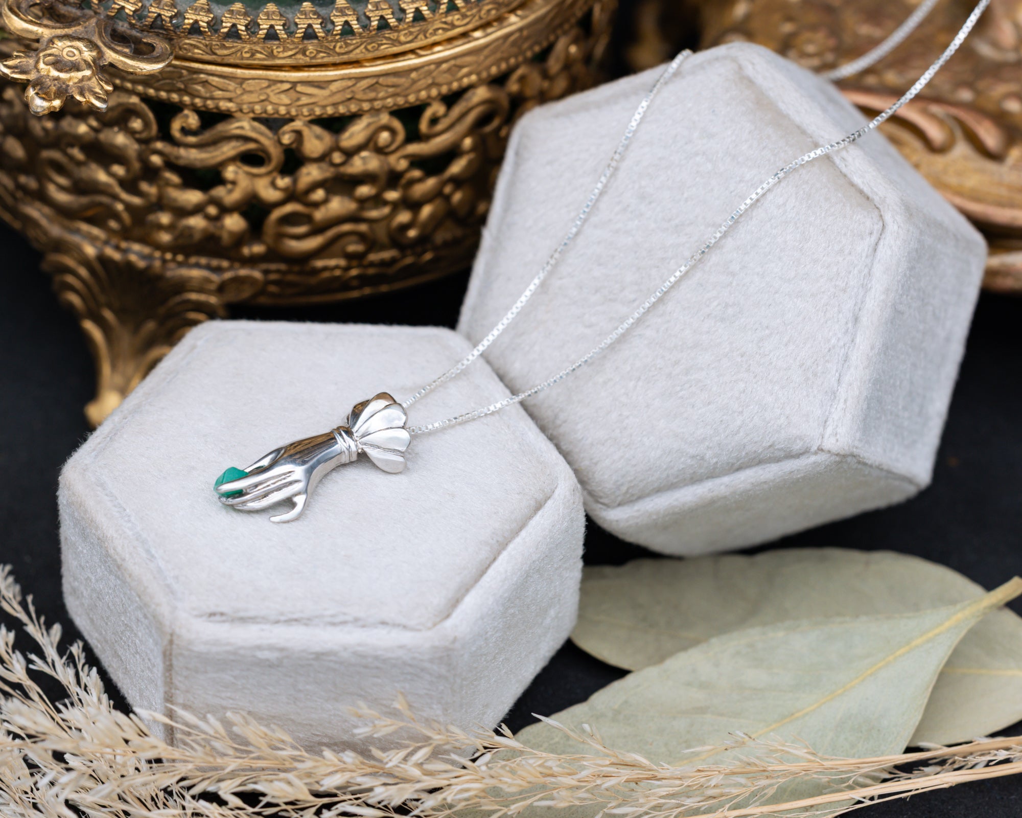 Silver necklace with a hand pendant on a white hexagonal jewelry box against a dark background.