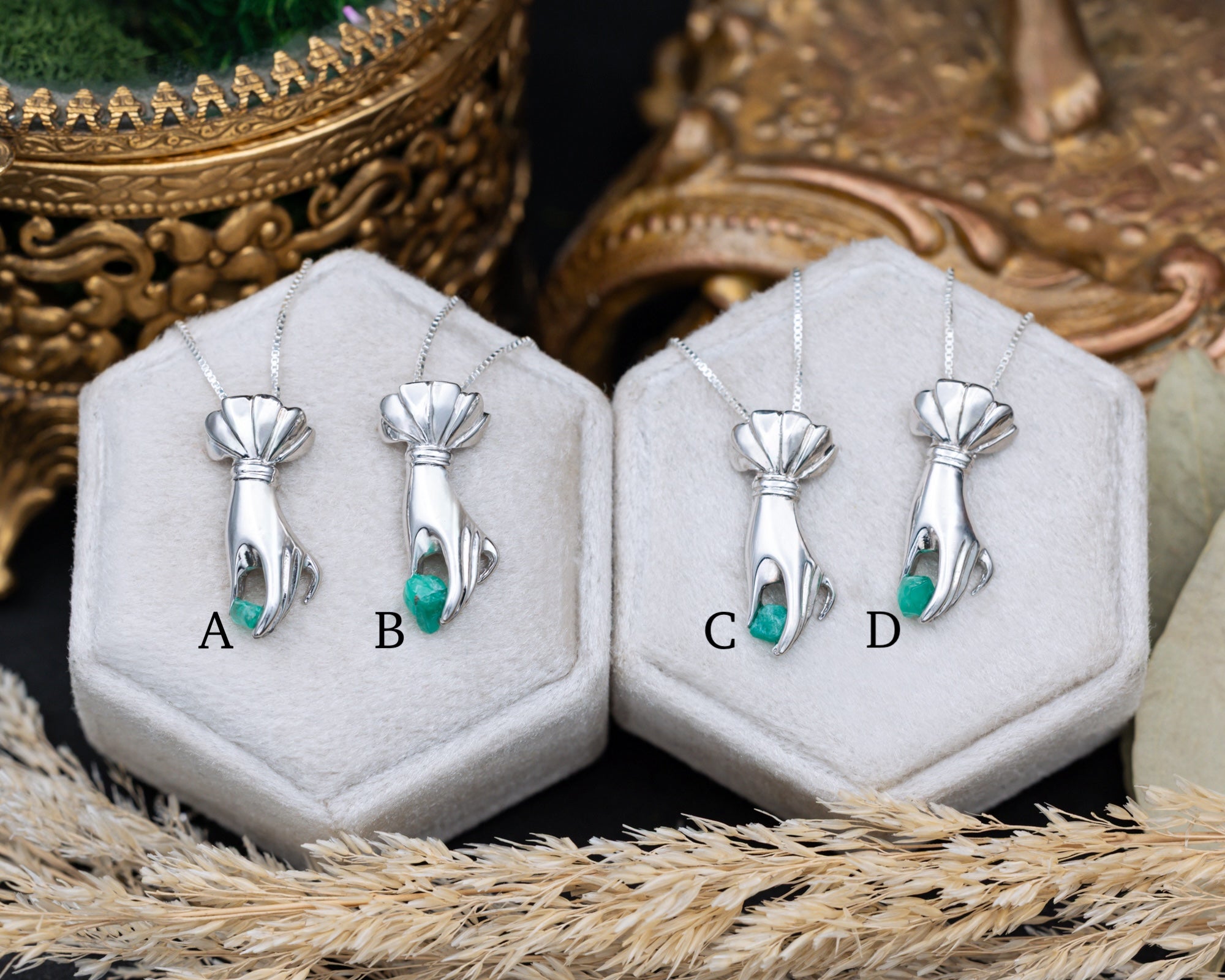 Silver pendants with raw emerald in hexagonal display cases on a textured surface.