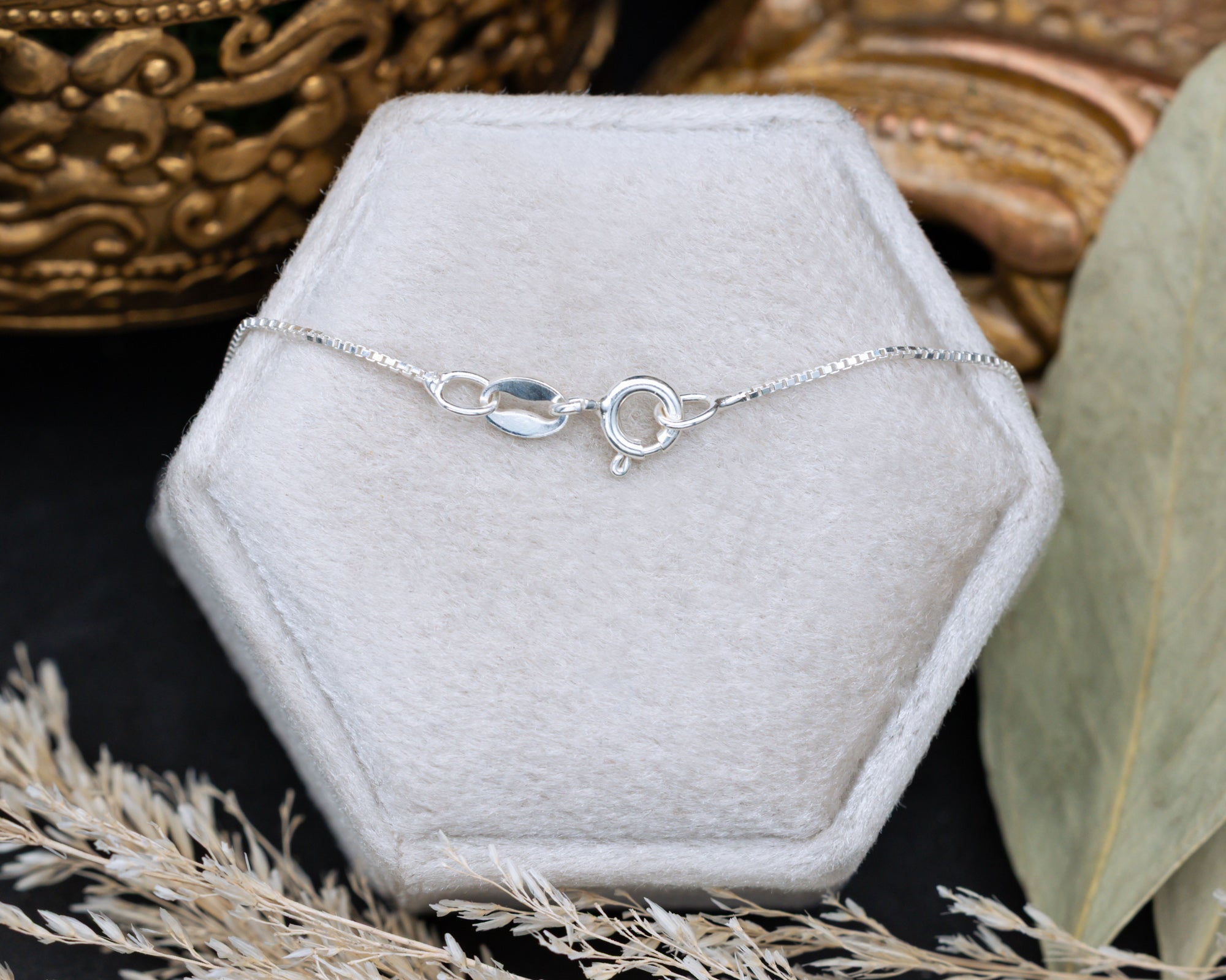 Silver spring clasp and chain on a hexagonal gray velvet stand.