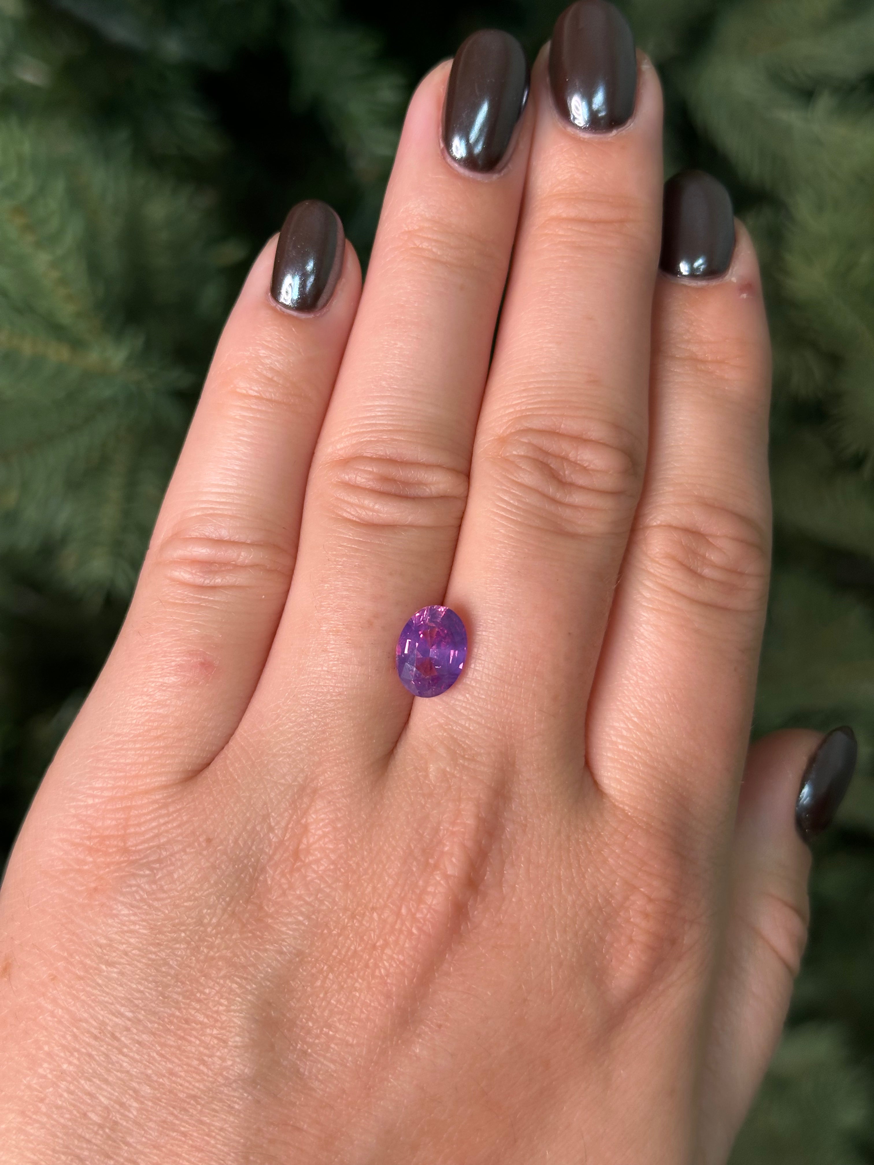 Hand with a purple sapphire sitting on fingers against a blurred green background