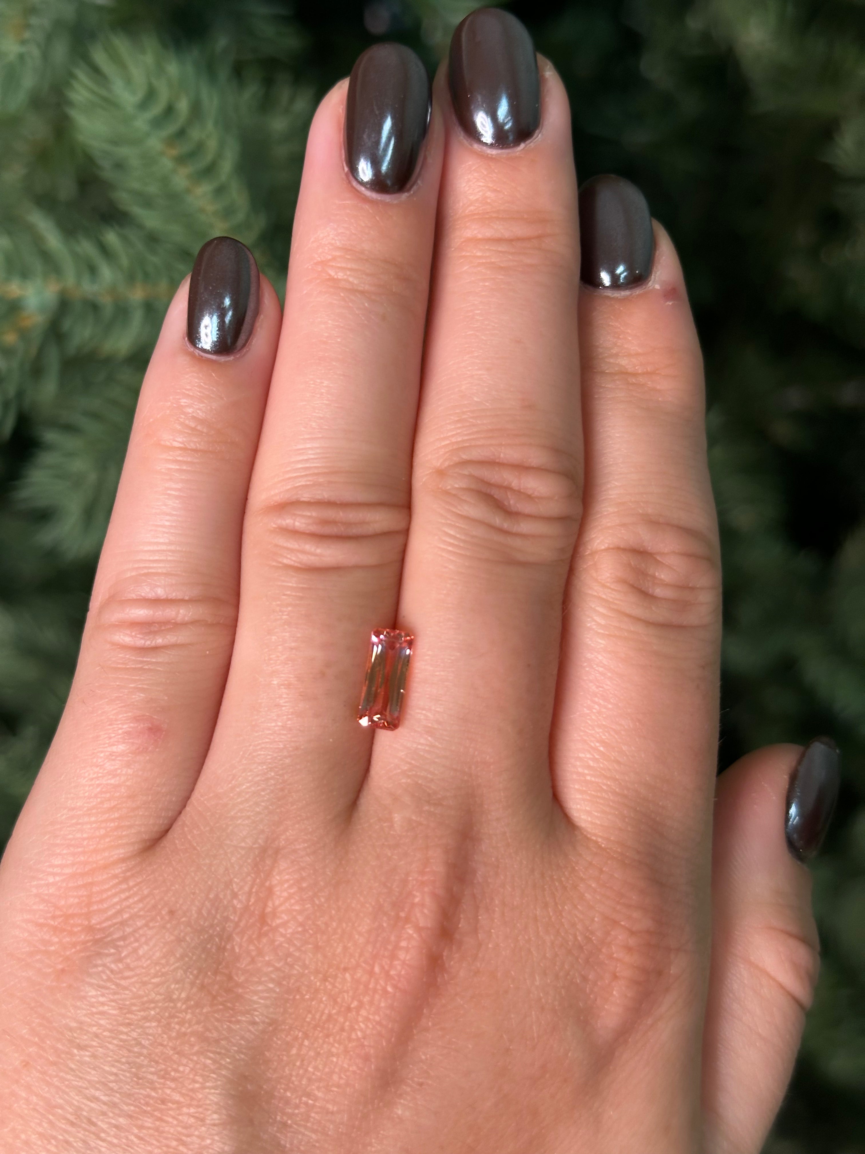 Hand with a peach sapphire sitting on fingers against a blurred green background