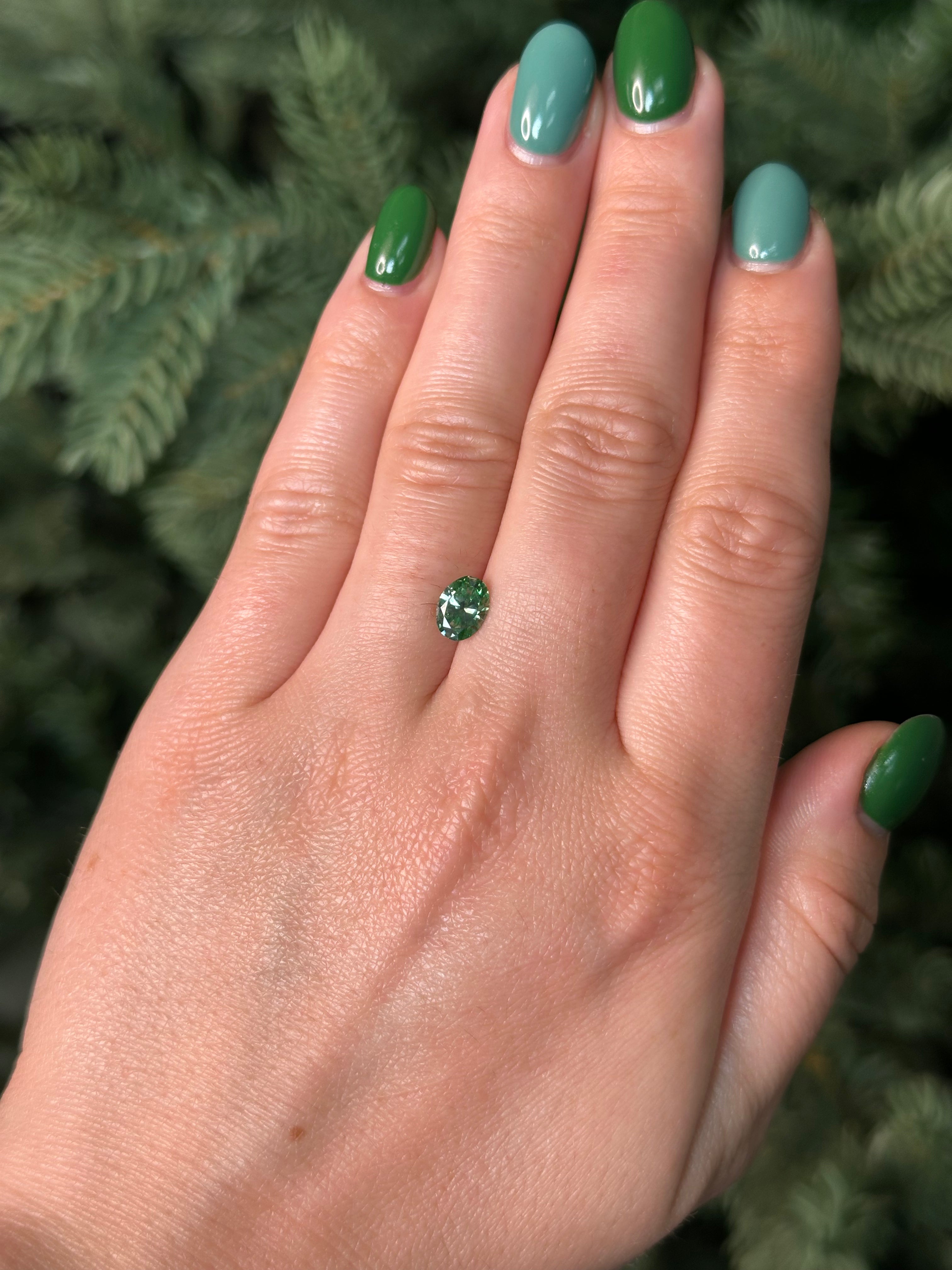 Hand with green nail polish holding a small green diamond against a blurred natural background