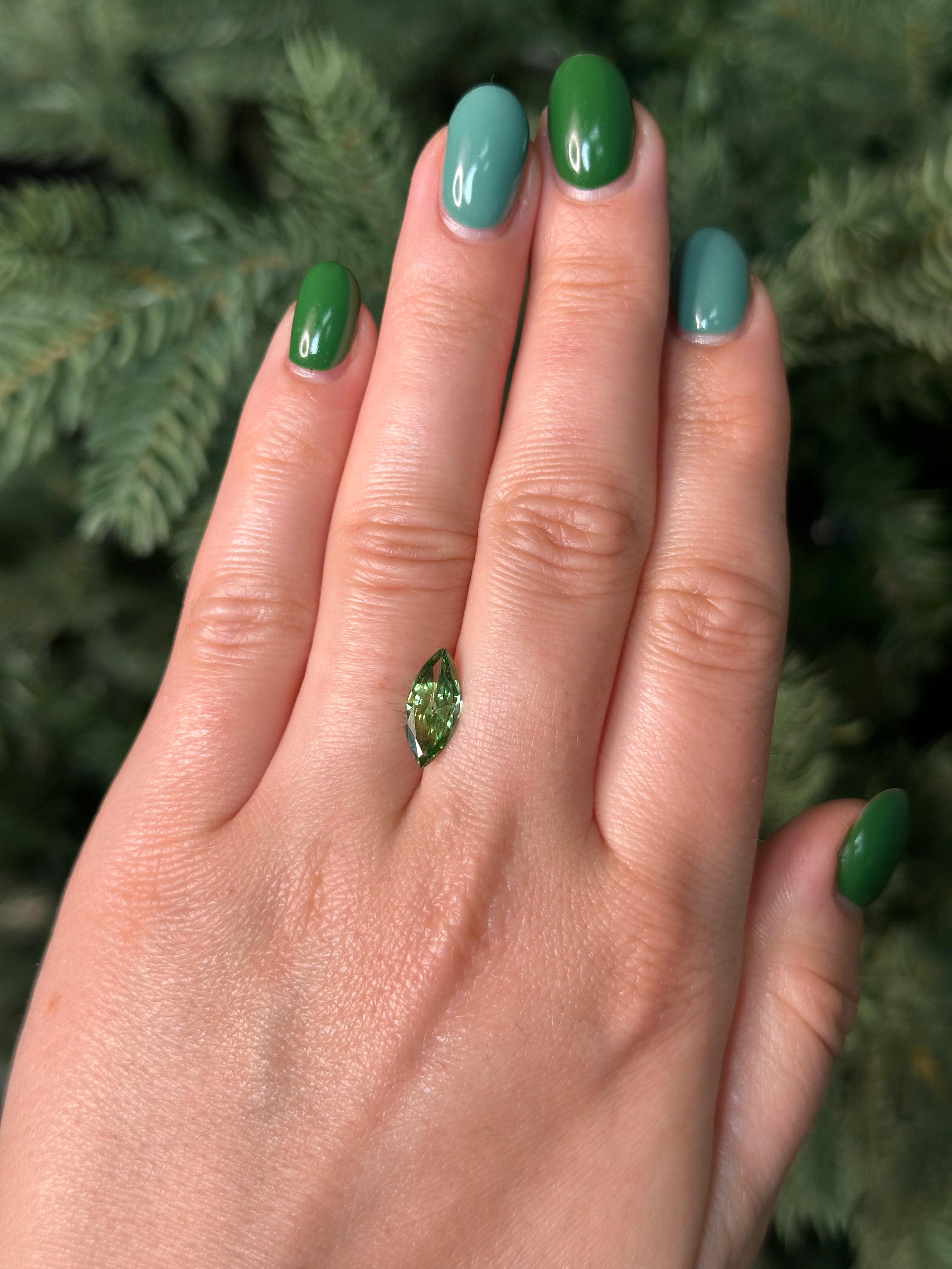 Hand with green nail polish holding a small green diamond against a blurred natural background