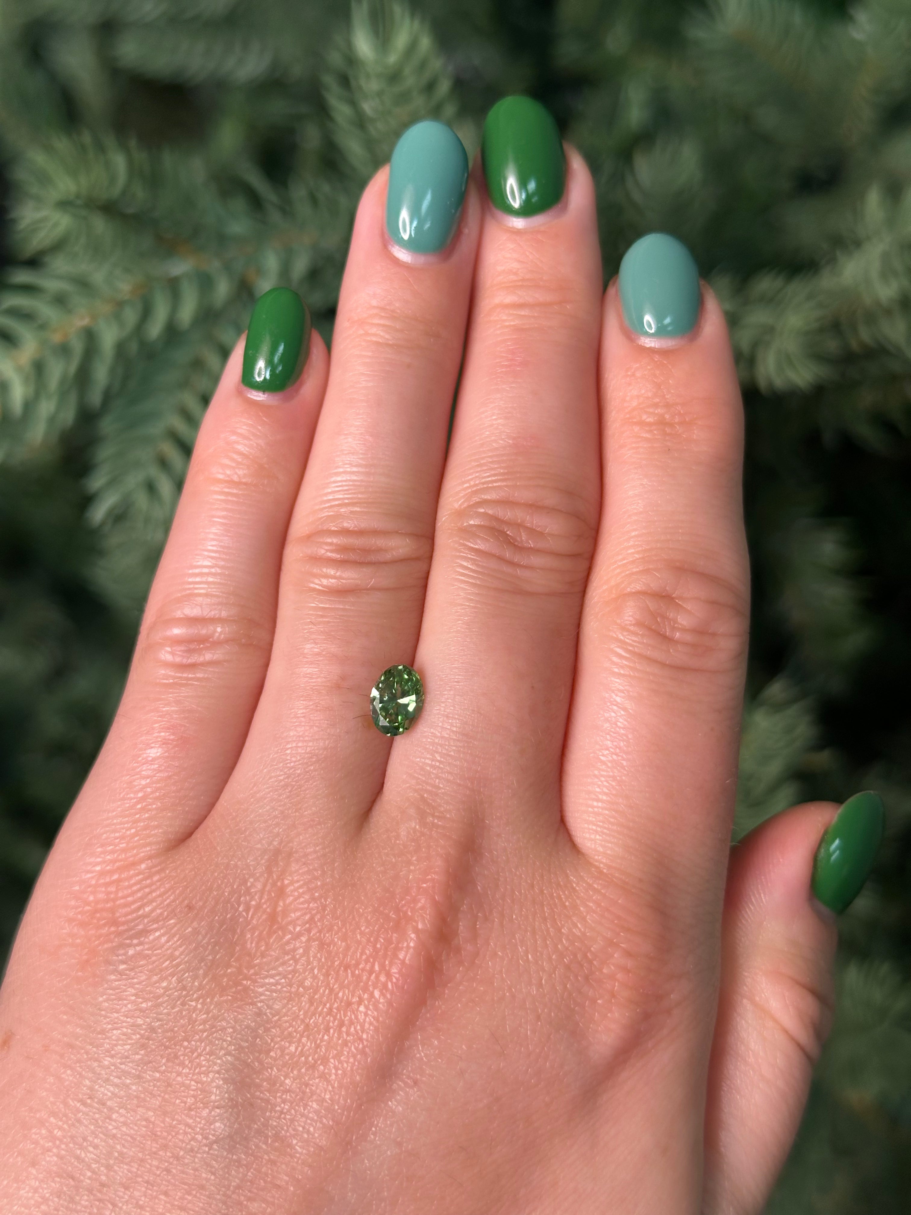 Hand with green nail polish holding a small green gemstone against a blurred natural background