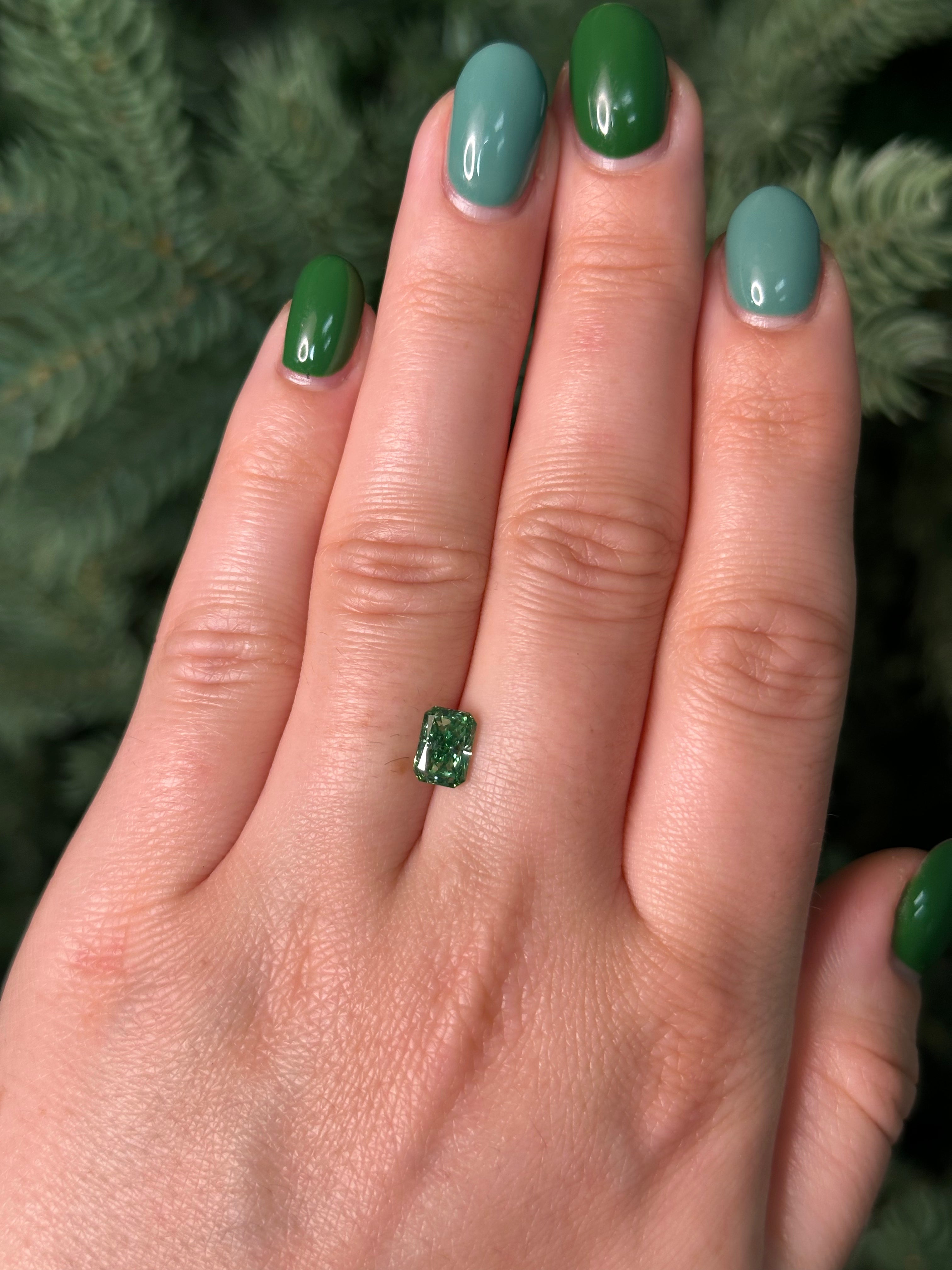 Hand with green nail polish holding a green diamond against a blurred natural background
