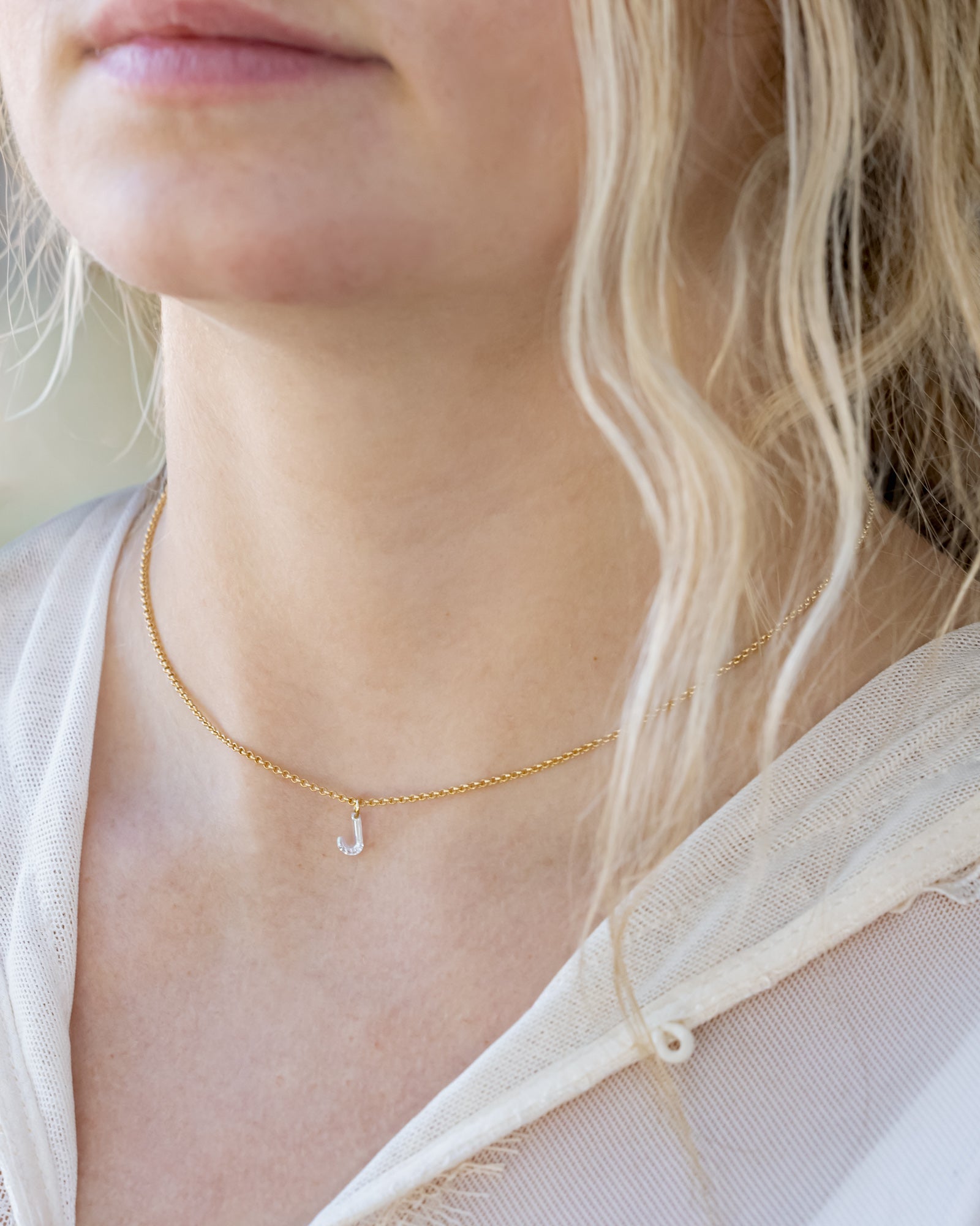Gold necklace with a small initial pendant worn by a person with blonde hair.