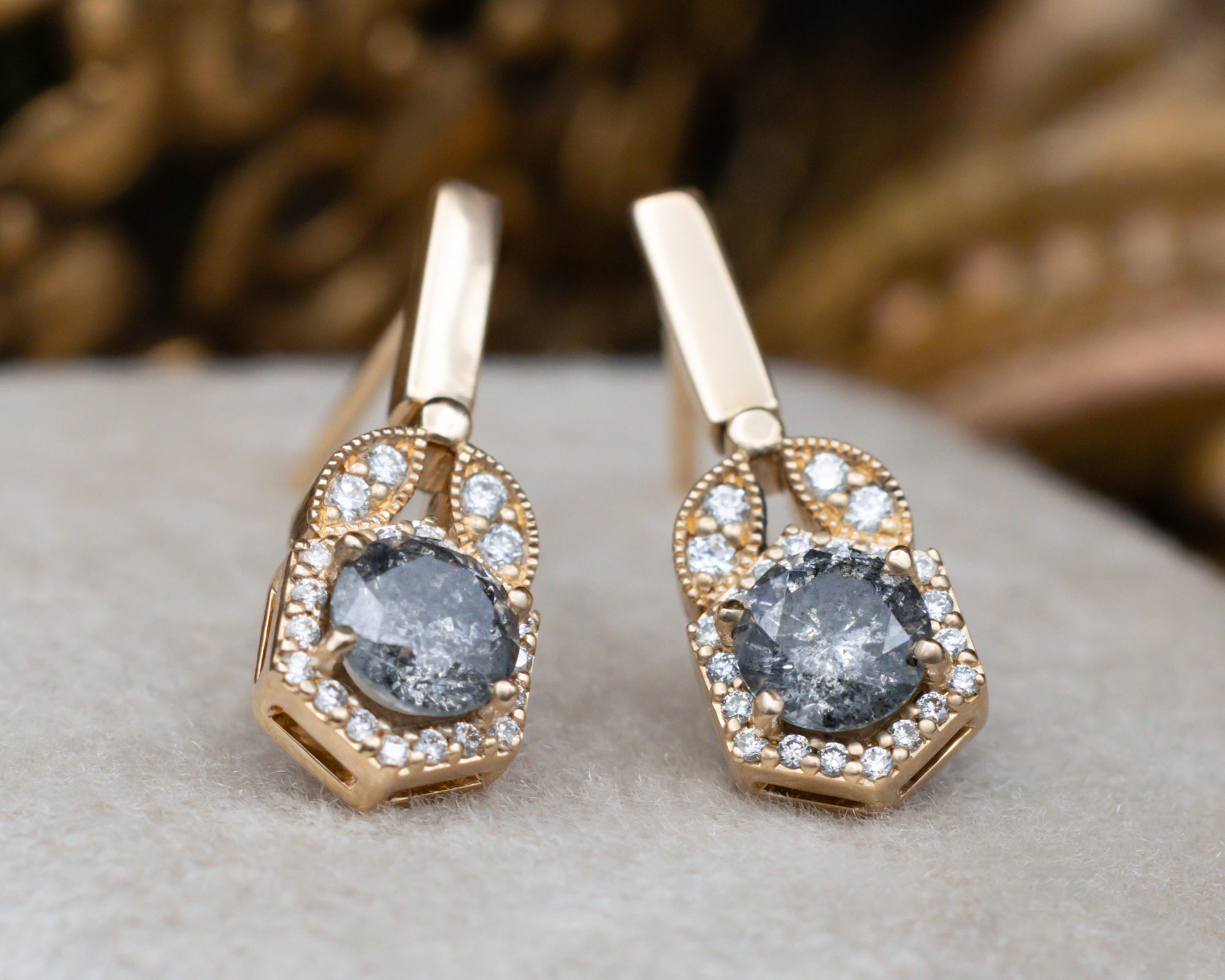Gold earrings with salt and pepper diamond centerstones in a hexagonal jewelry box.