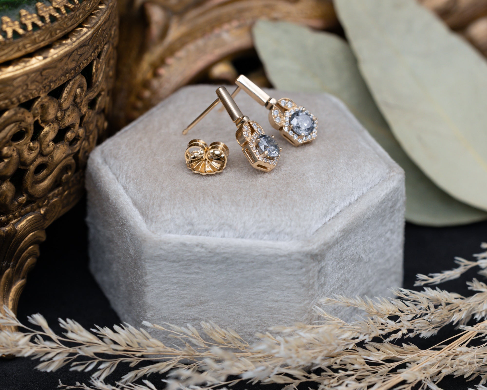 Gold earrings with salt and pepper diamond centerstones in a hexagonal jewelry box.