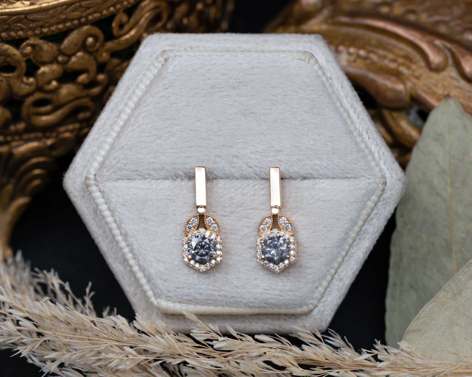 Gold earrings with salt and pepper diamond centerstones in a hexagonal jewelry box.