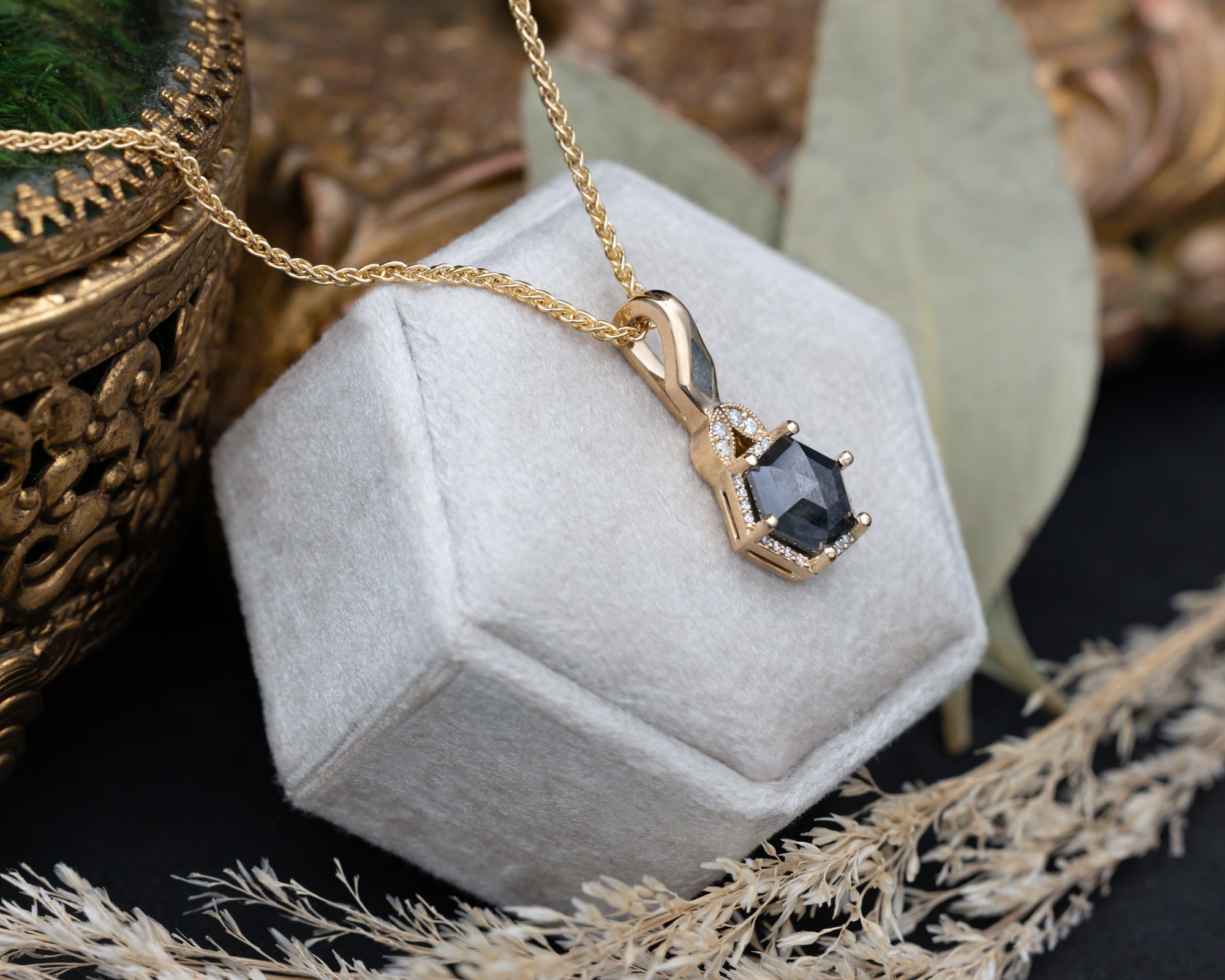 Gold necklace with a salt & pepper diamond pendant on a hexagonal gray velvet stand.