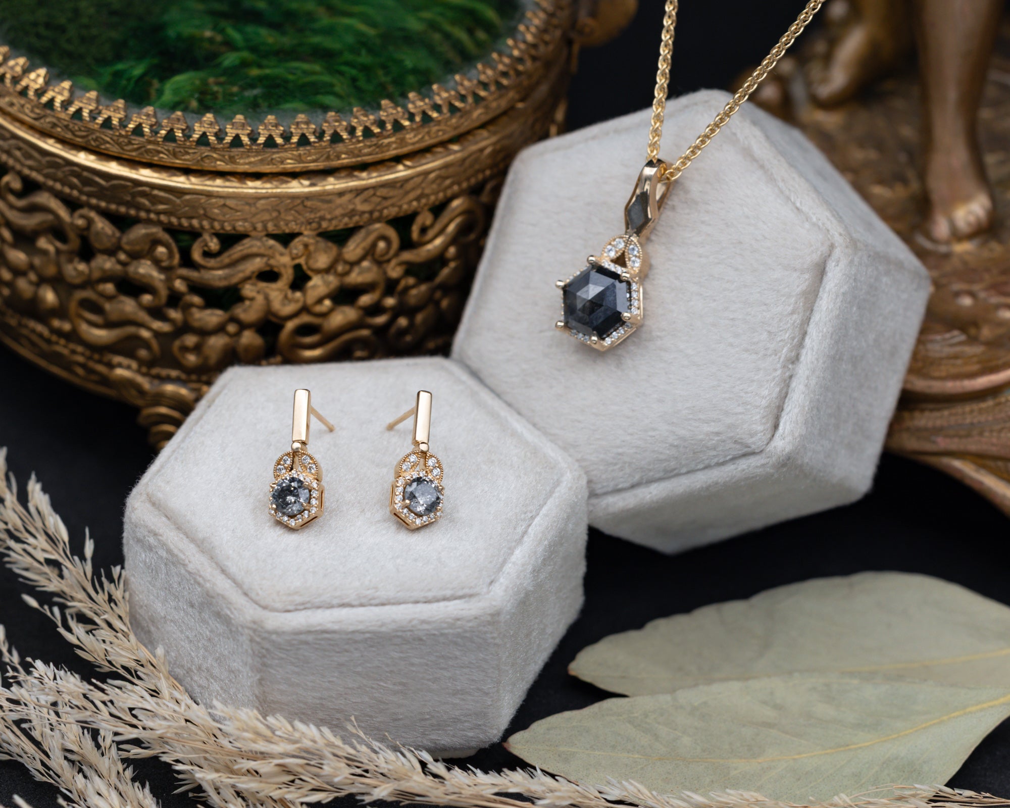 Gold earrings and necklace with salt & pepper diamond centerstones on hexagonal display stands.