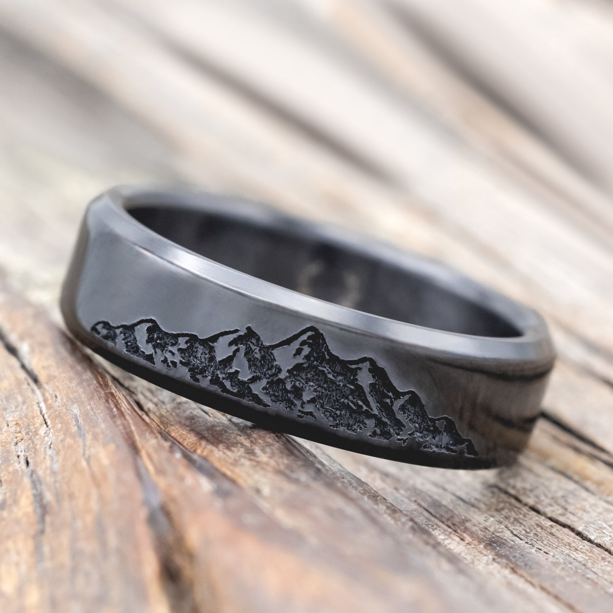 Black zirconium ring with mountain engraving on a wooden surface