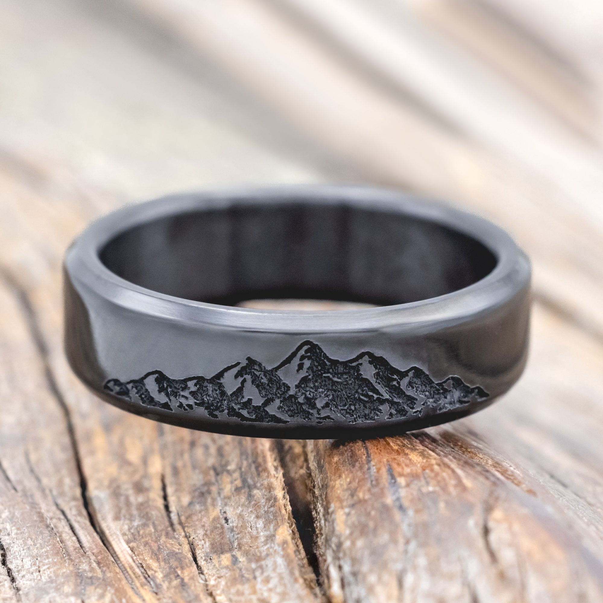Black zirconium ring with mountain engraving on a wooden surface