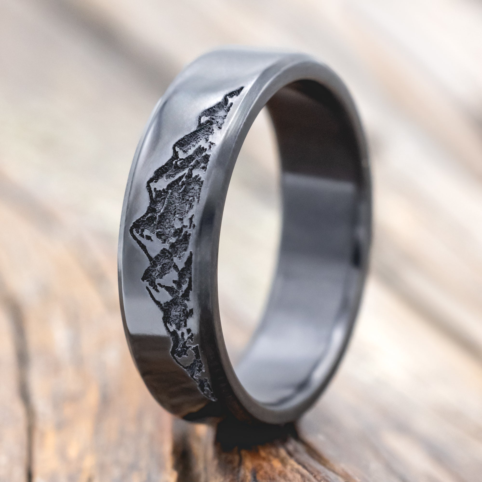 Black zirconium ring with mountain engraving on a wooden surface