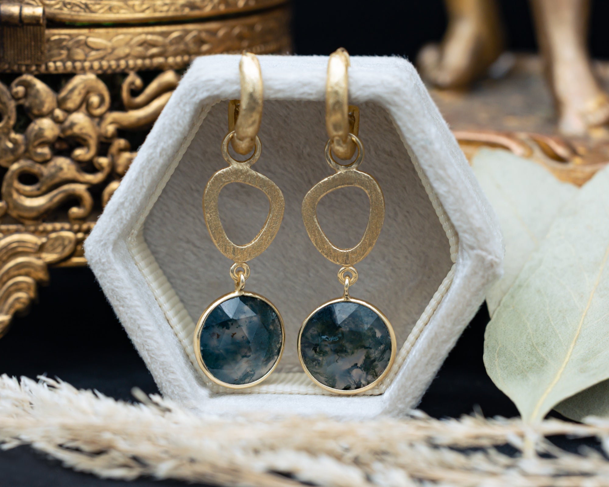 Gold earrings with moss agate on a hexagonal jewelry display