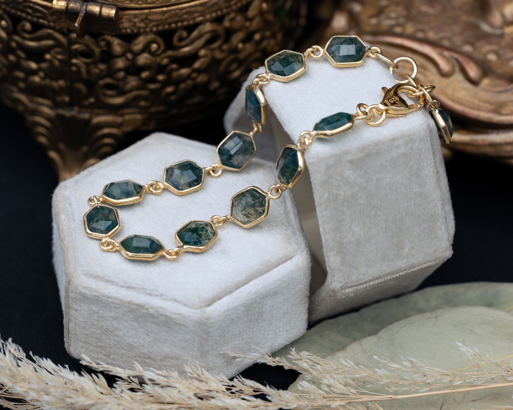 Gold bracelet with hexagon moss agate on a white stand with decorative background
