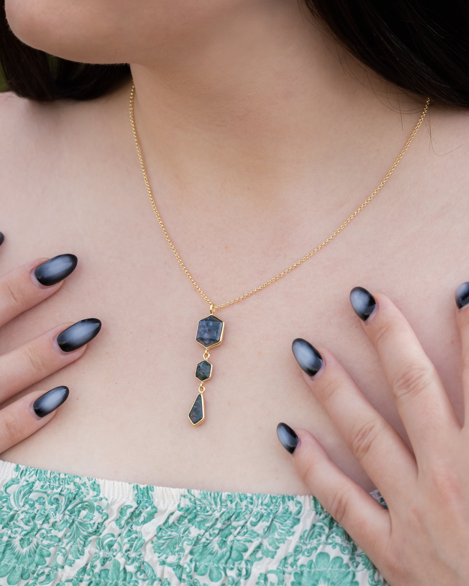 Necklace with moss agate and gold chain worn by a person wearing dark nail polish