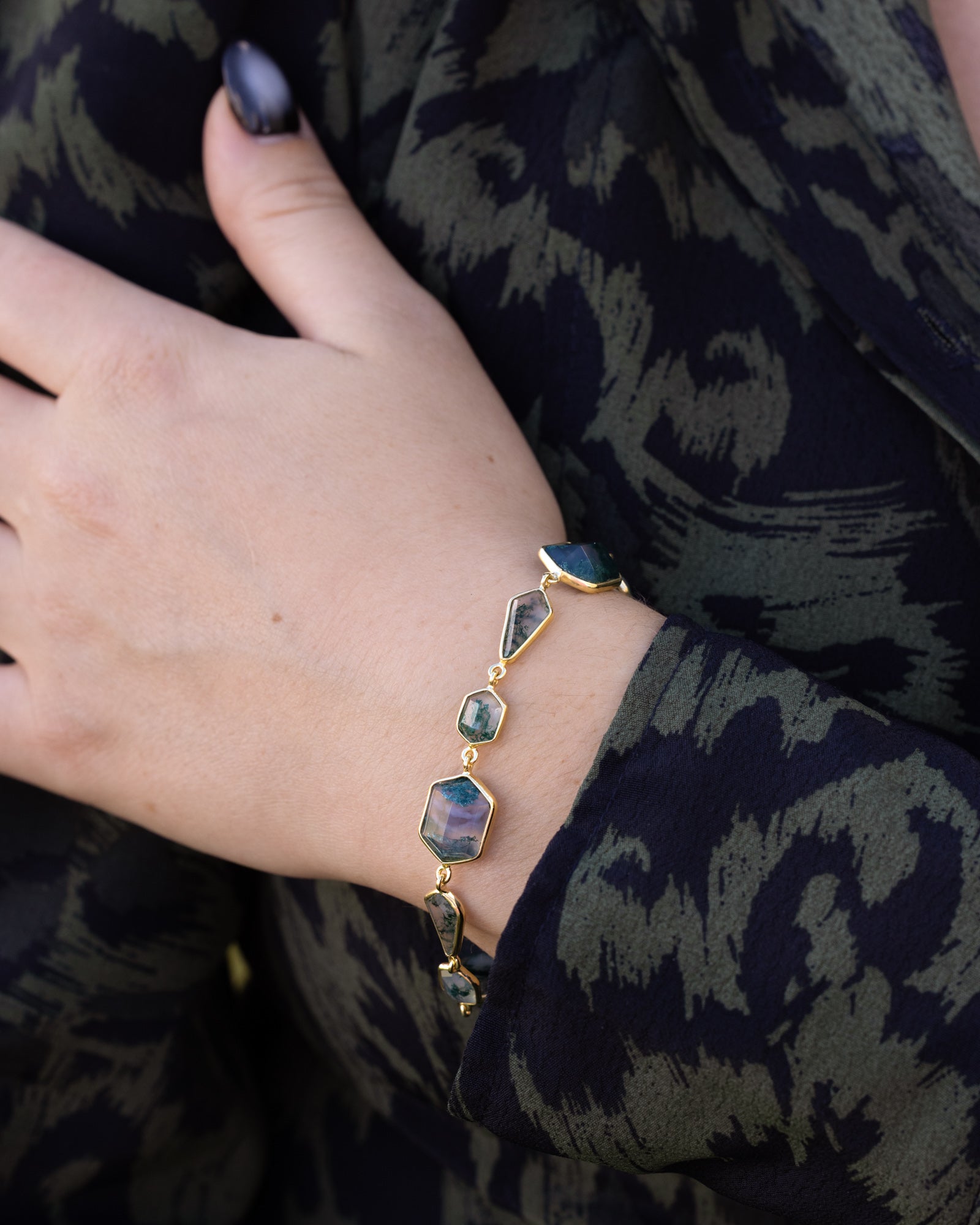 Bracelet with gemstones on a wrist against a dark patterned fabric background