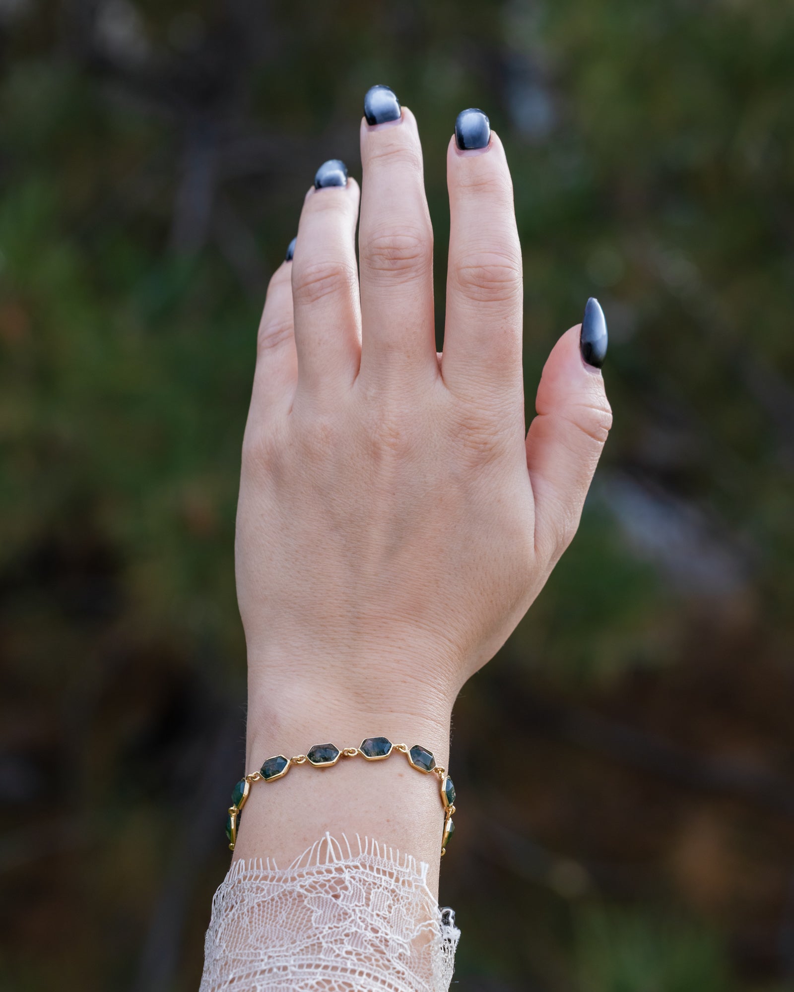 Hand with gold moss agate bracelet against a blurred natural background