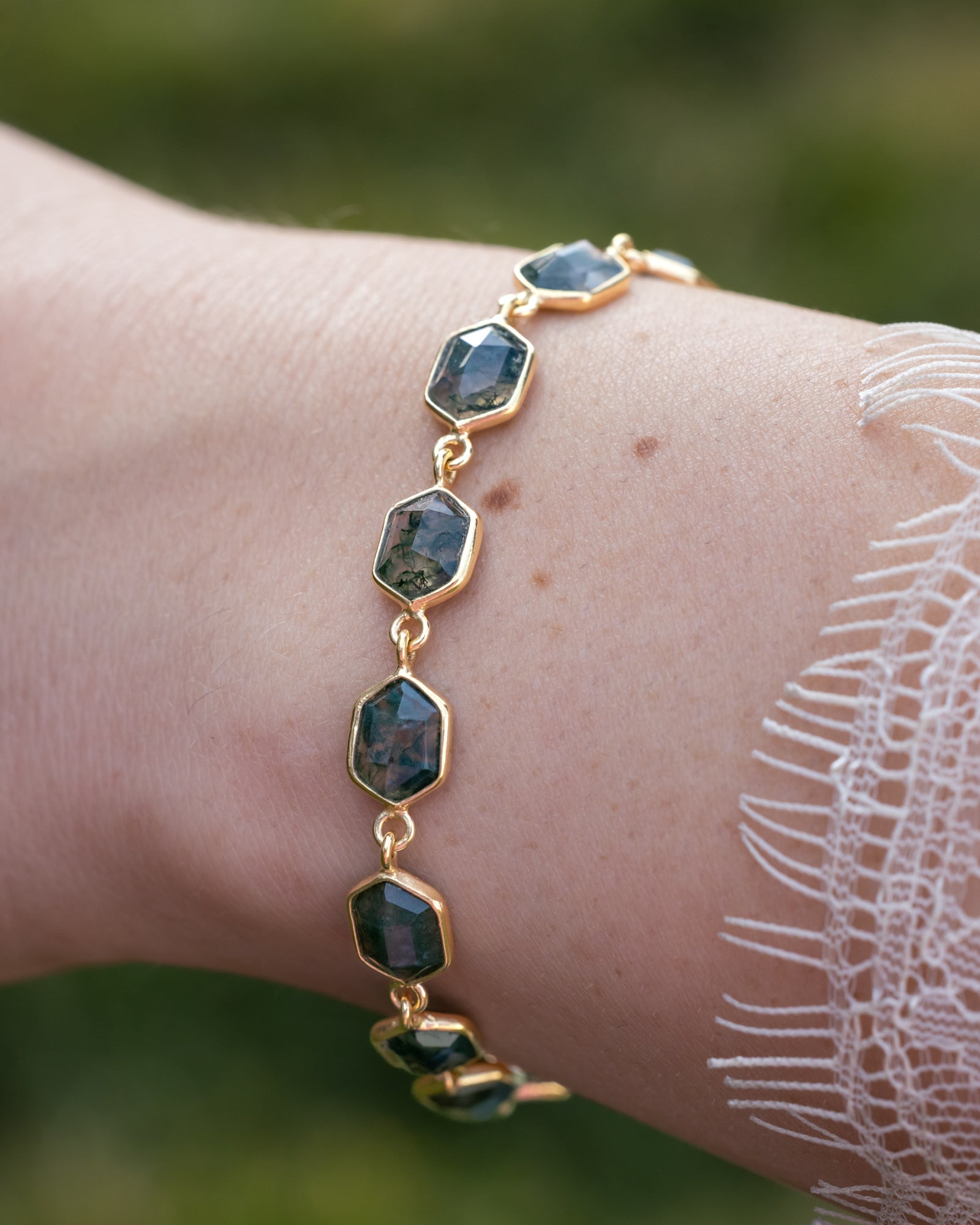 Gold bracelet with moss agate on a wrist against a blurred natural background