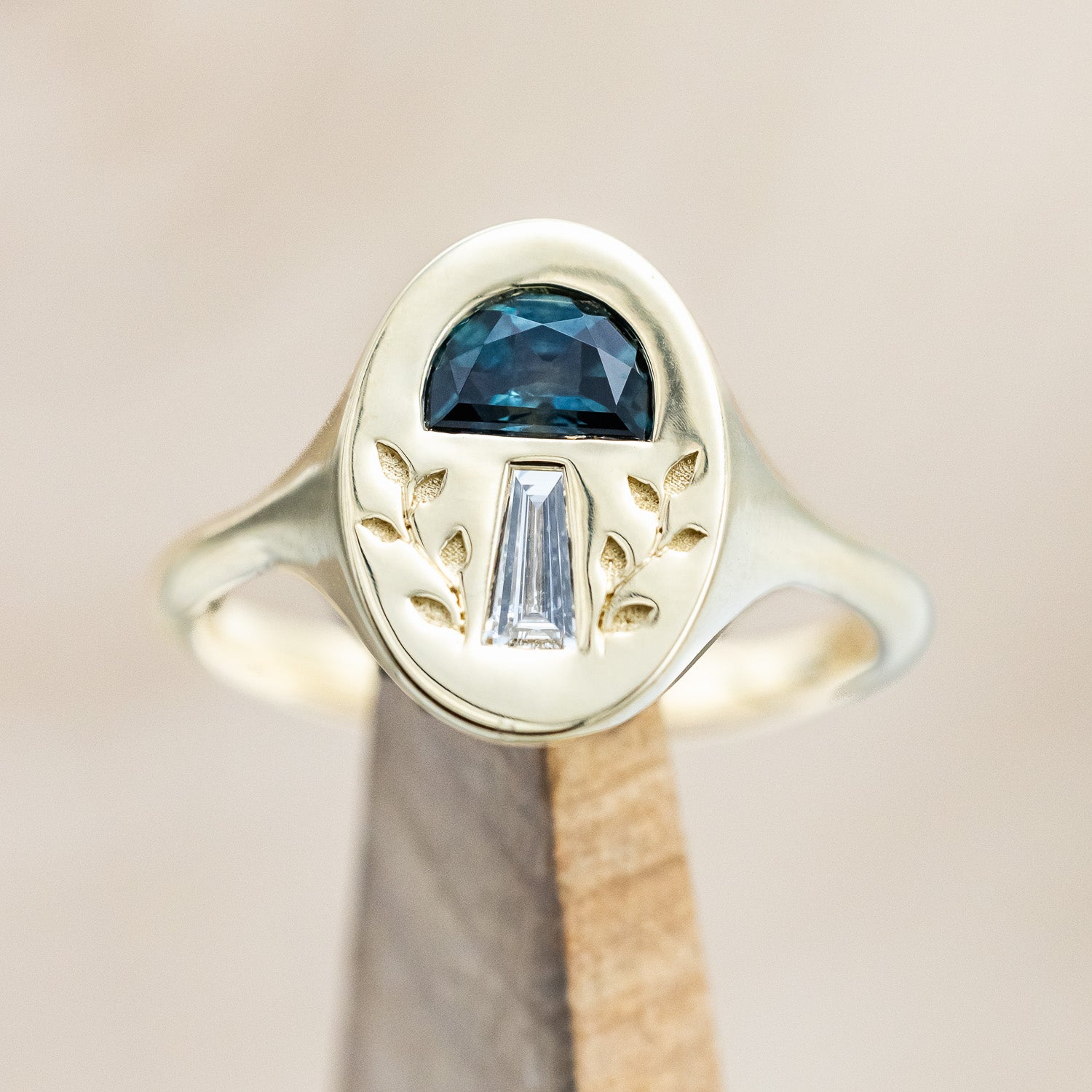 A 14K yellow gold signet ring with a half moon gem cap, tapered baguette diamond stem, and vines engraved on both sides.
