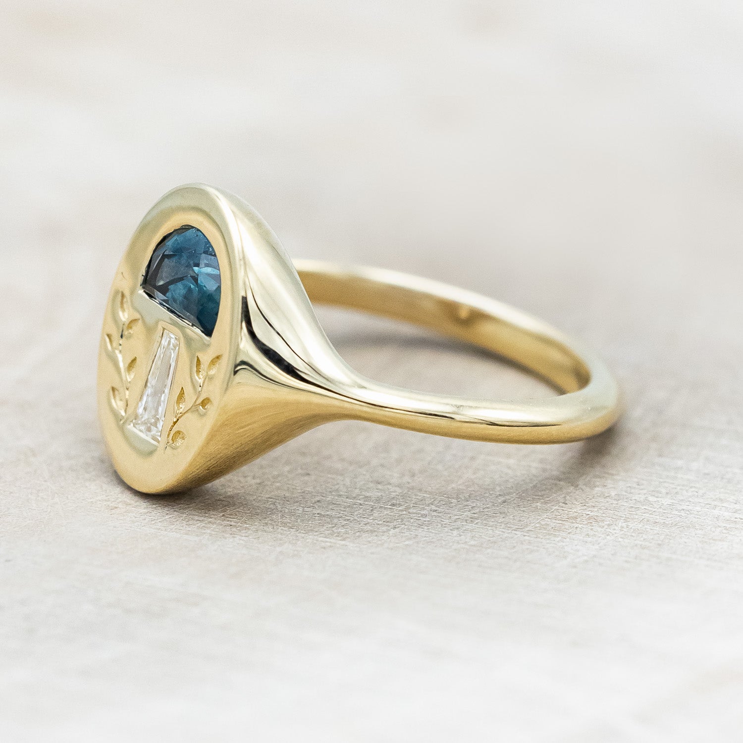 Side profile of a 14K yellow gold signet ring with a half moon gem cap, tapered baguette diamond stem, and vines engraved on both sides.